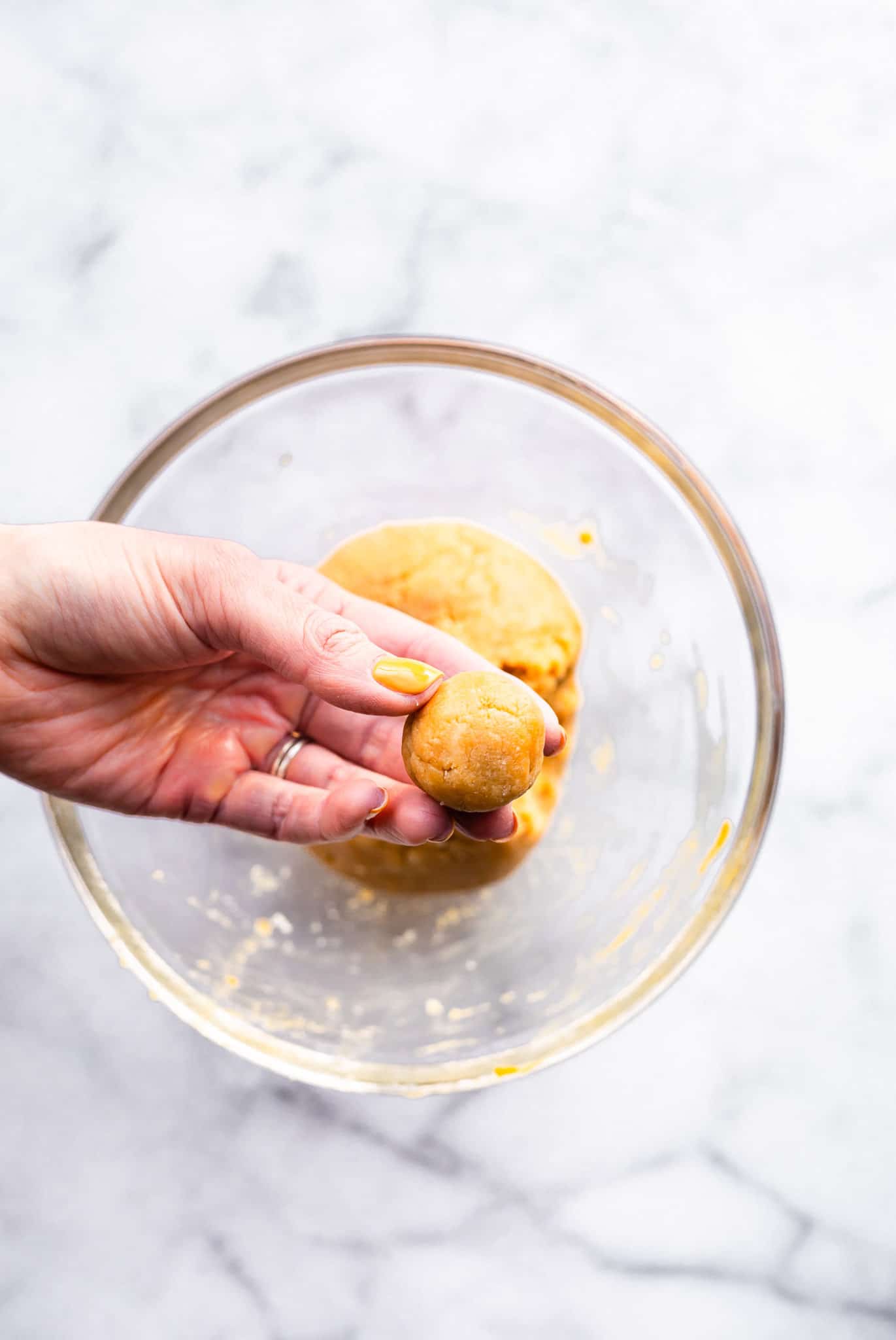 a woman's hand holidng a formed cake ball over glass bowl of cake ball batter