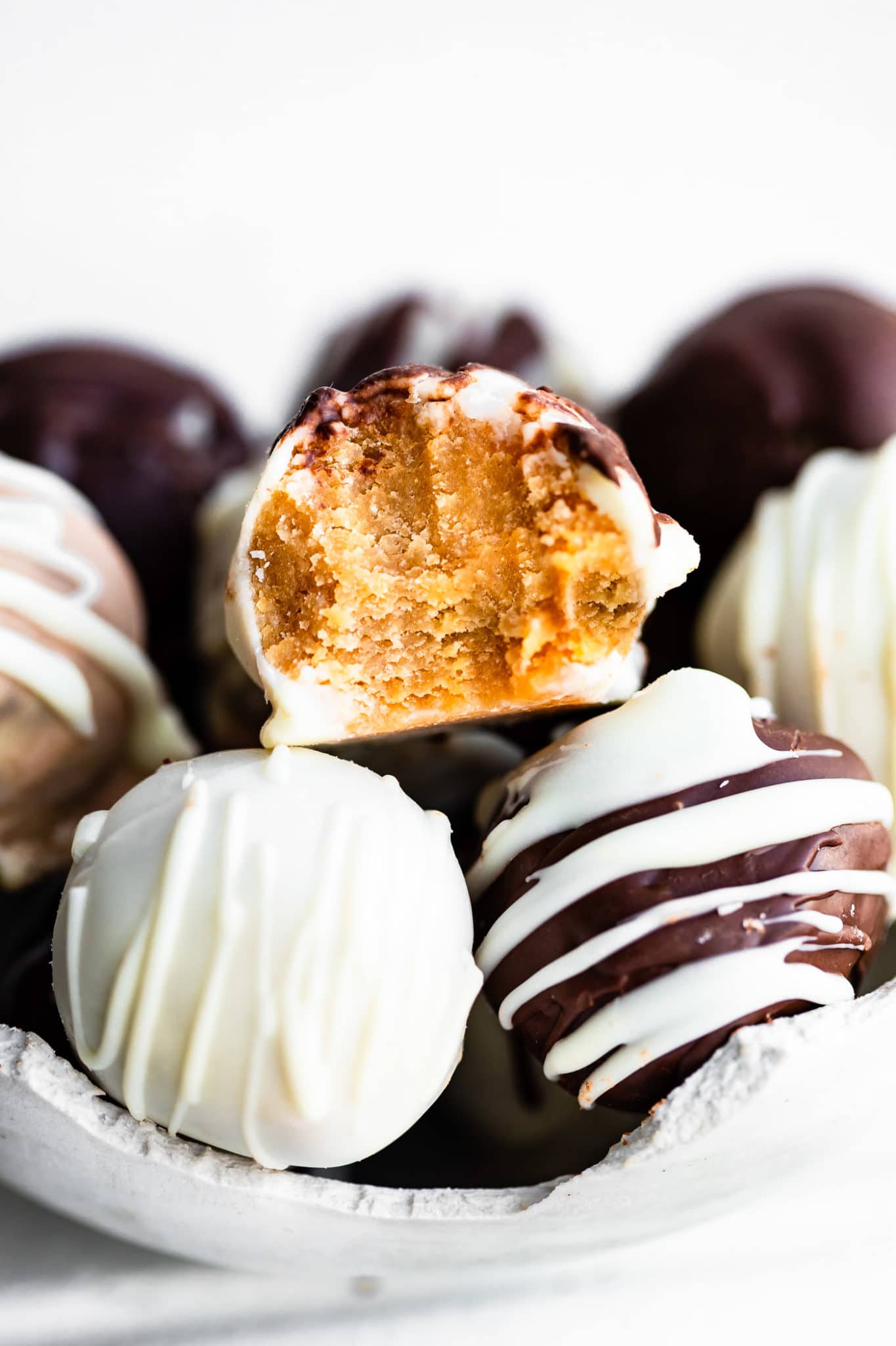 a side image of a carrot cake ball with a bite taken out of it sitting on top of other cake balls that have been coated with white and dark chocolate