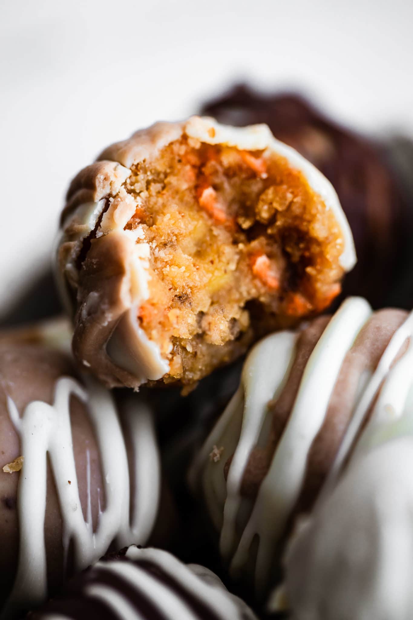 a carrot cake cake ball with a bite taken out of it on top of a pile of various cake balls coated with chocolate
