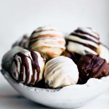 a white bowl holding chocolate cake balls, carrot cake balls, and vanilla cake balls that have been coated in white and dark chocolate