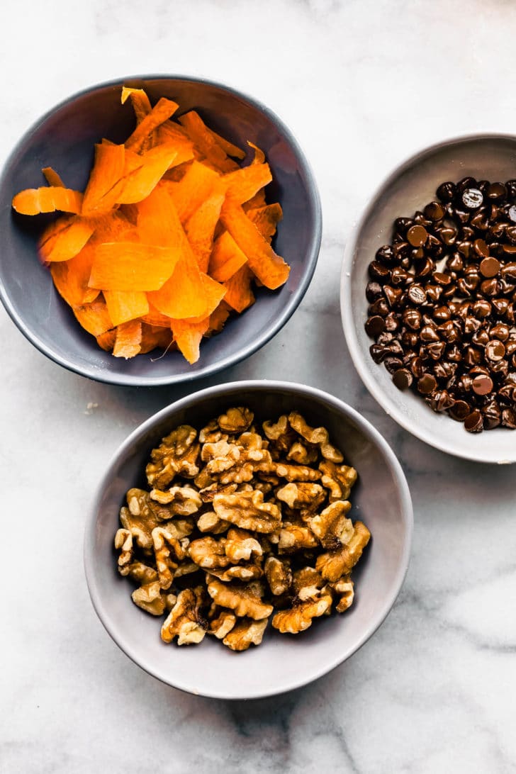 3 bowls containing shredded carrots, walnuts, and chocolate chips to make a carrot cake balls recipe