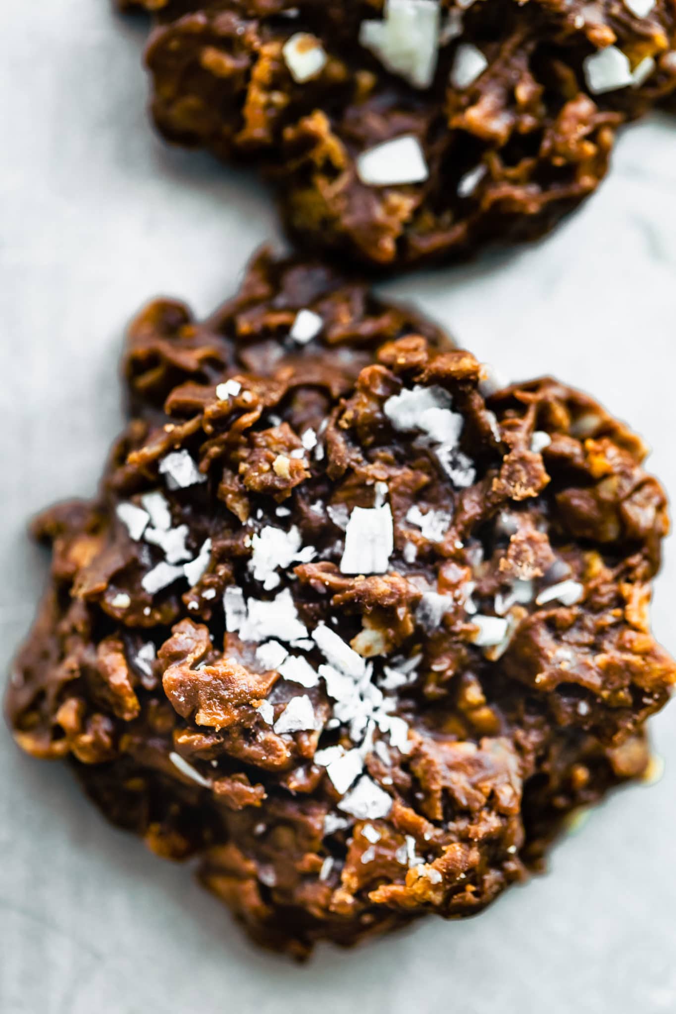 a close up image of a chocolate peanut butter cornflake cookie topped with coconut flakes and sea salt
