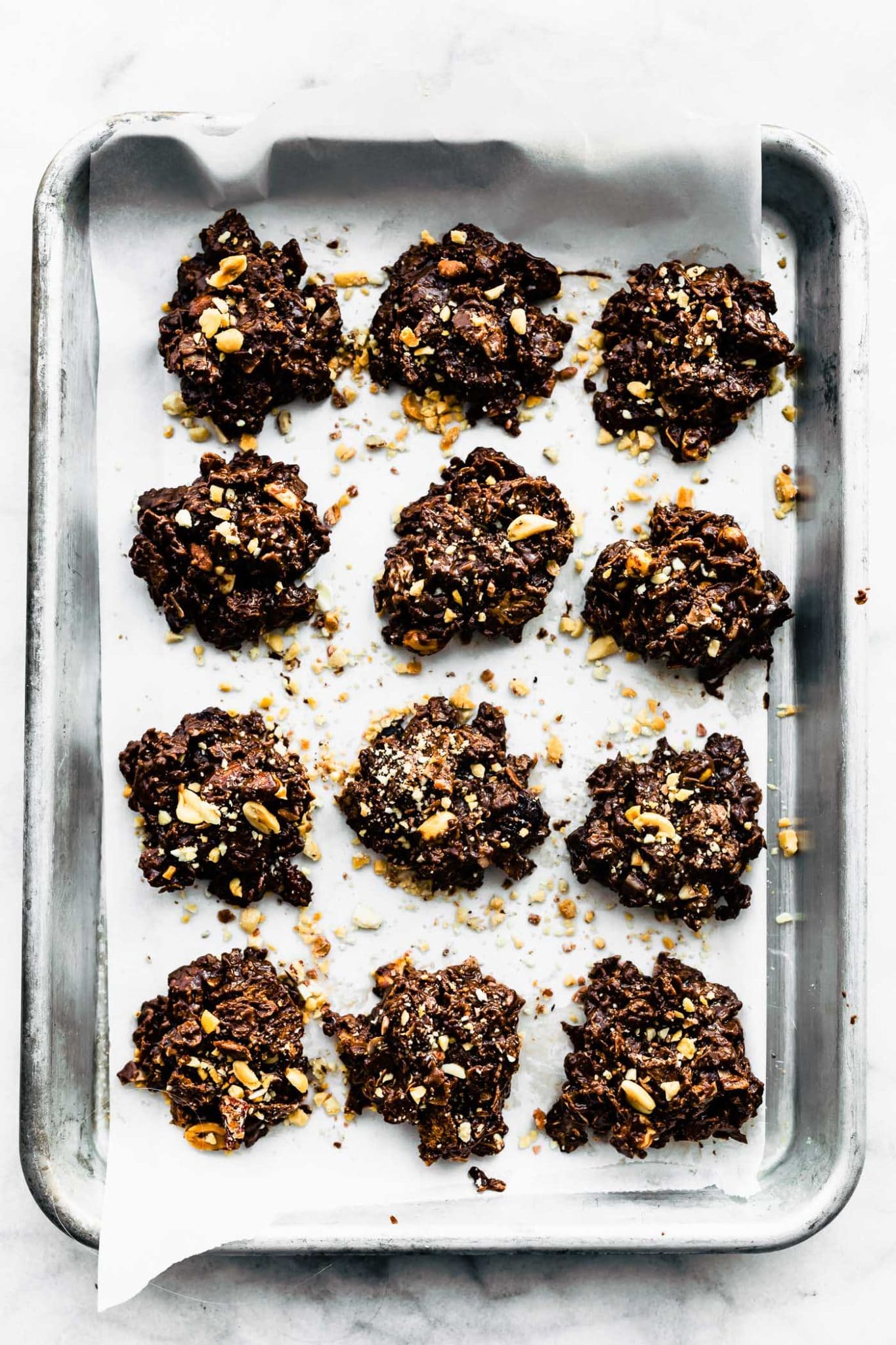 12 chocolate peanut butter cornflake cookies on a baking sheet topped with coocnut flakes, sea salt, and chopped nuts