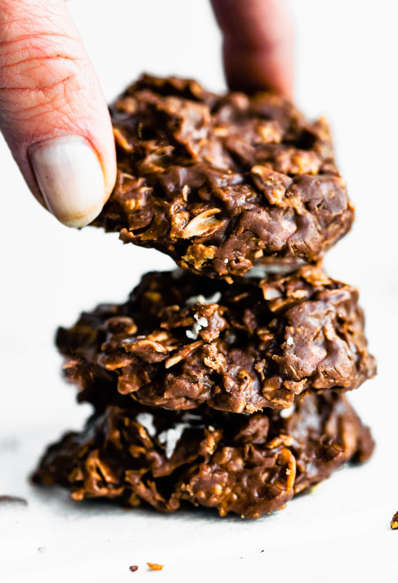 a woman's hand grabbing a chocolate peanut butter cornflake cookie off a pile of three cookies stacked on top of each other