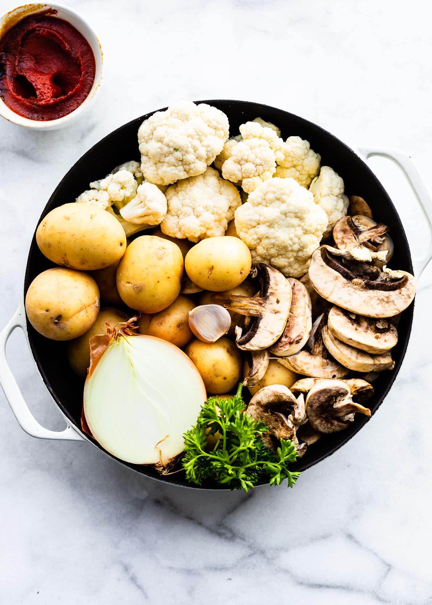 cauliflower florets, golden potatoes, half an onion, mushrooms, and fresh herbs in a sauce pan for potato and cauliflower shpeherd's pie