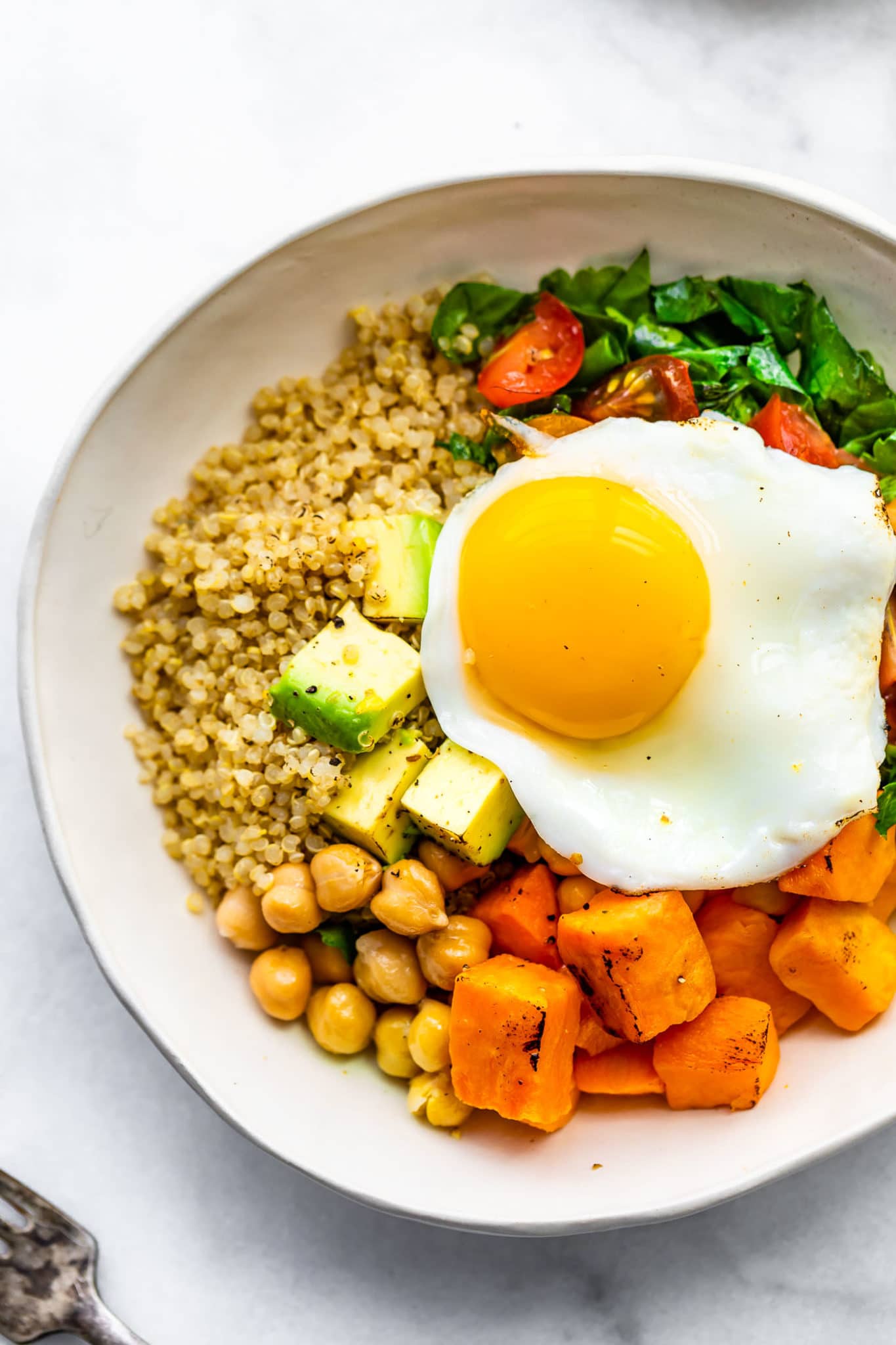 overhead image of a savory quinoa breakfast bowl with quinoa, chickpeas, sweet potatoes, spinach, tomatoes, avocado, and a fried egg