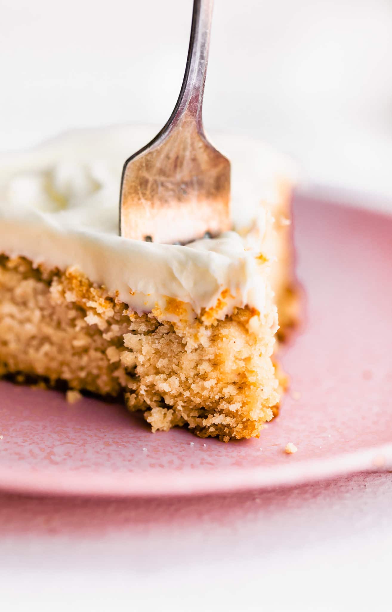 a fork stabbed straight down into a slice of vegan vanilla cake with vanilla frosting