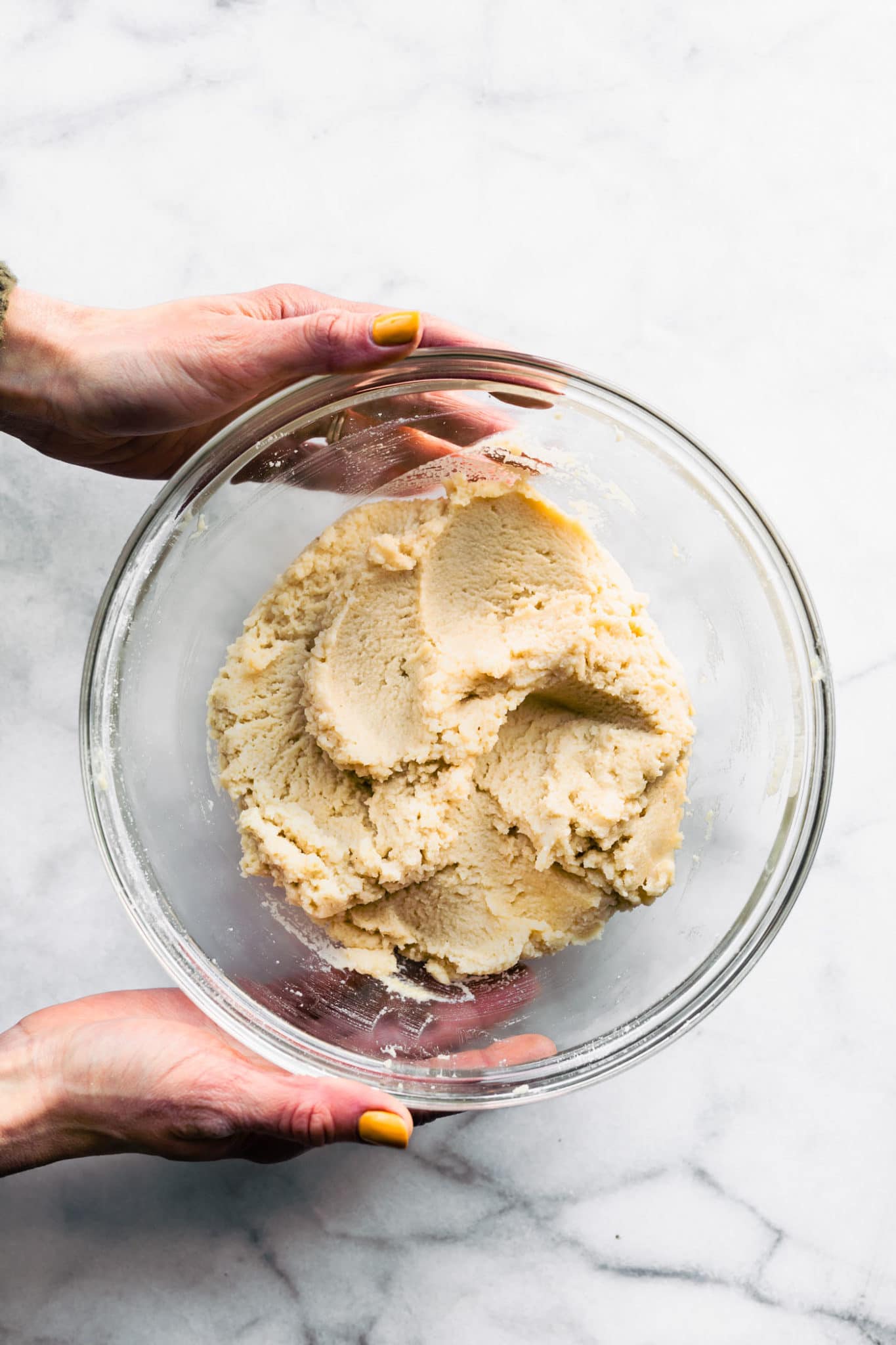 two hands holding a glass bowl with vegan vanilla cake batter