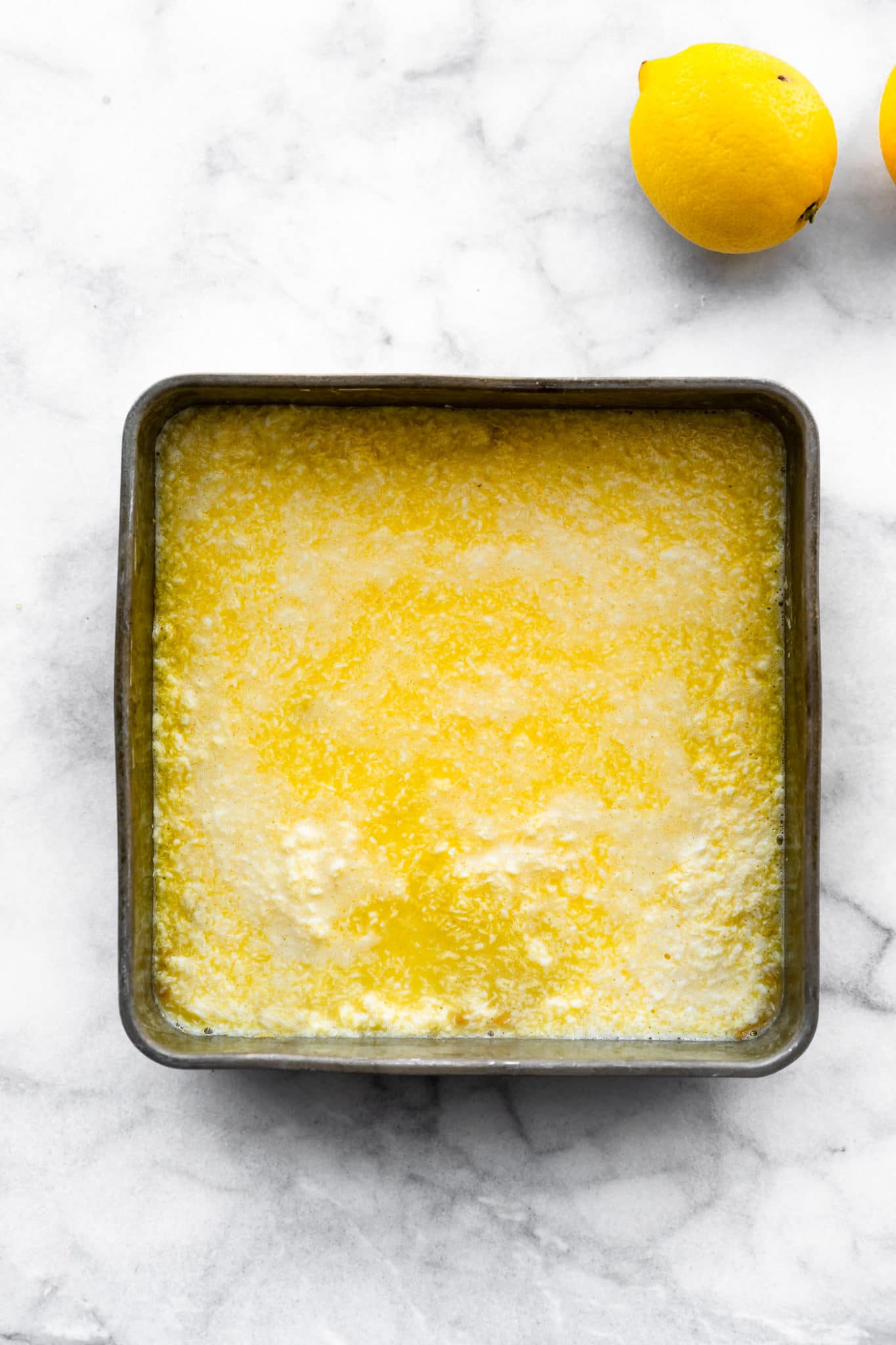 overhead image of raw lemon bars in a square baking dish with a lemon on the side