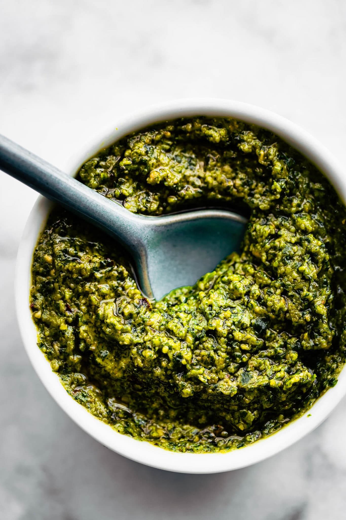 on overhead image of cilantro pesto in a white bowl with a blue spoon dipping in