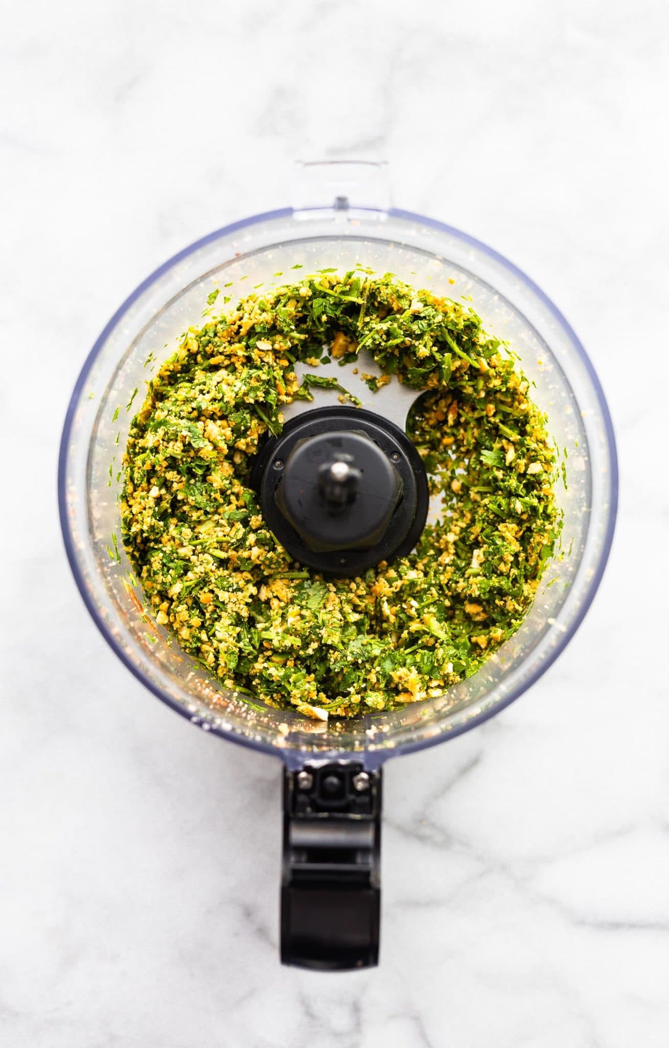 an overhead image of ingredients for cilantro pesto in a food processor before olive oil is added