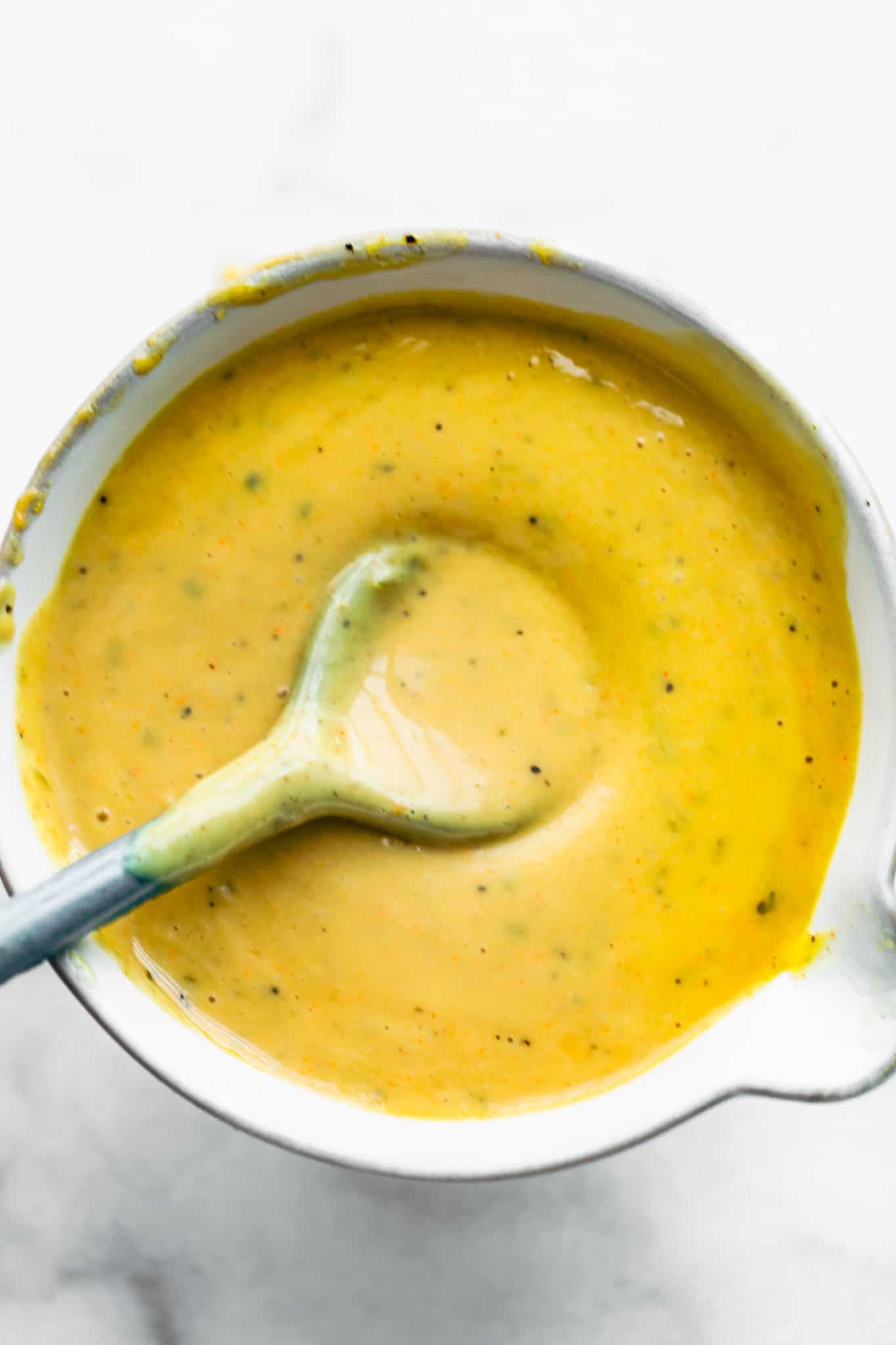overhead image of a small white bowl full of creamy mustard sauce with a sauce spoon dipping into it