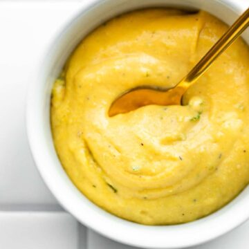 overhead image of a golden spoon dipping into a small white bowl full of creamy mustard sauce