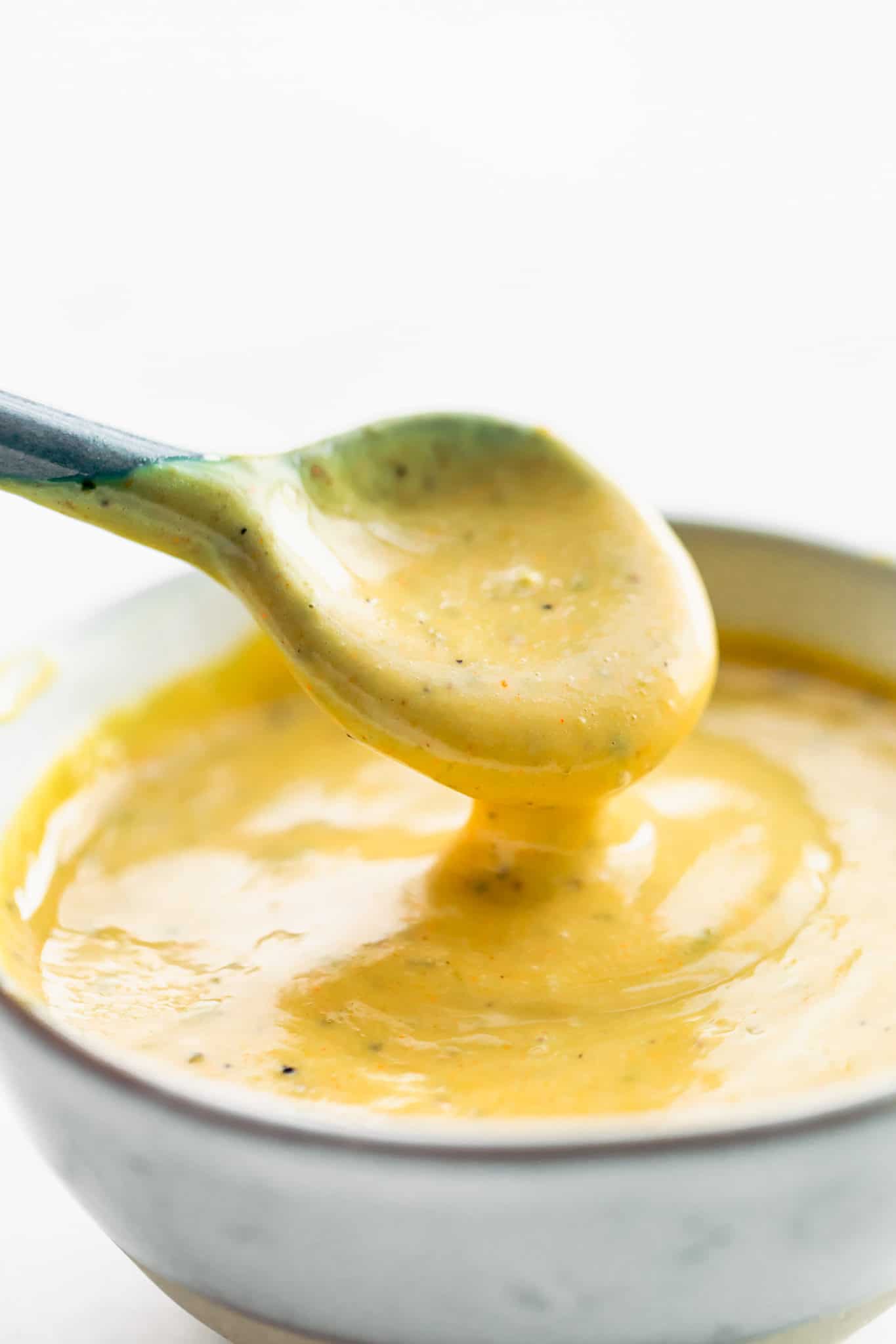 side image of a small sauce spoon dipping into a white bowl full of creamy mustard sauce