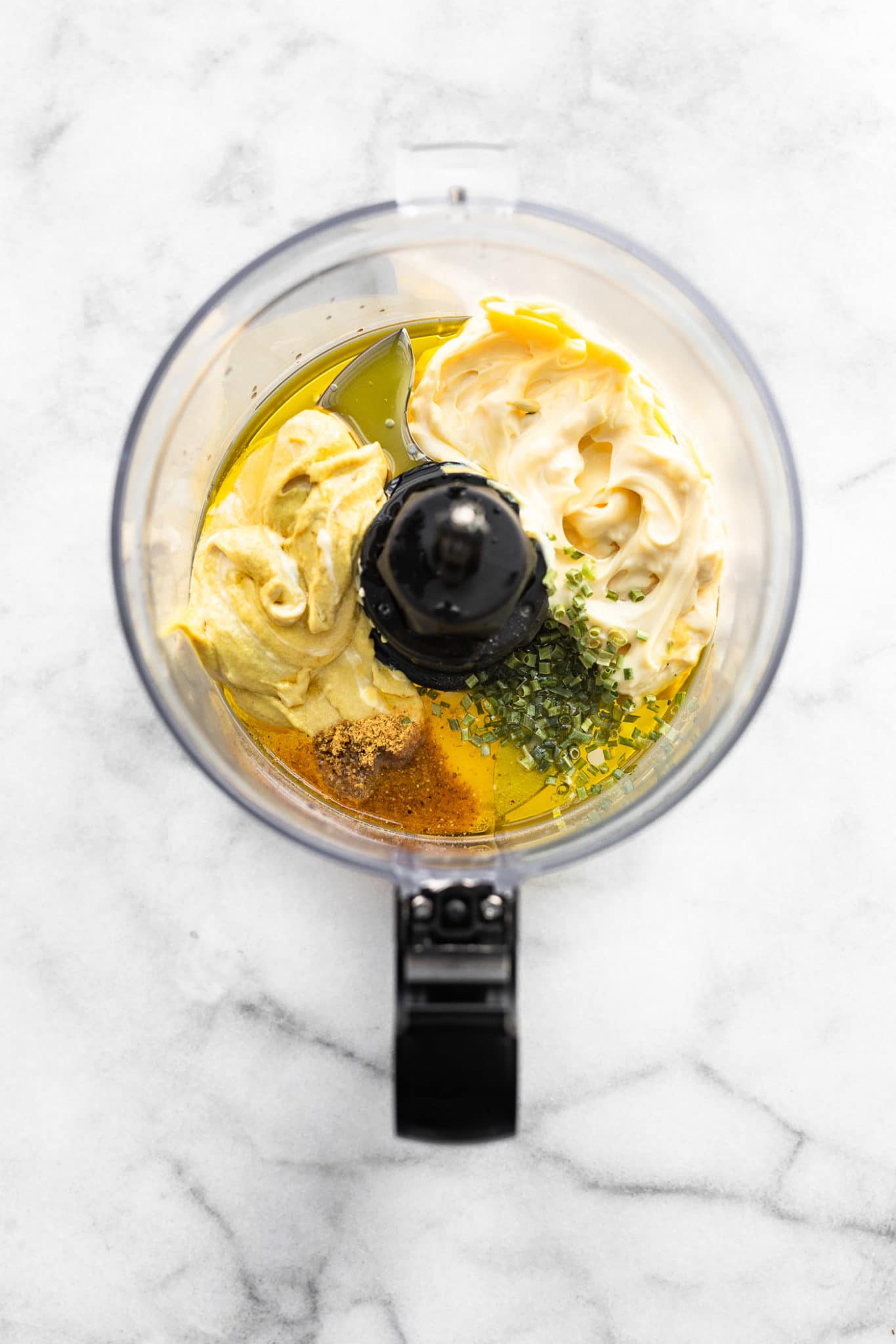 overhead image of a food processor full of dijon mustard, mayo, olive oil, fresh herbs, and spices to make a homemade creamy mustard sauce