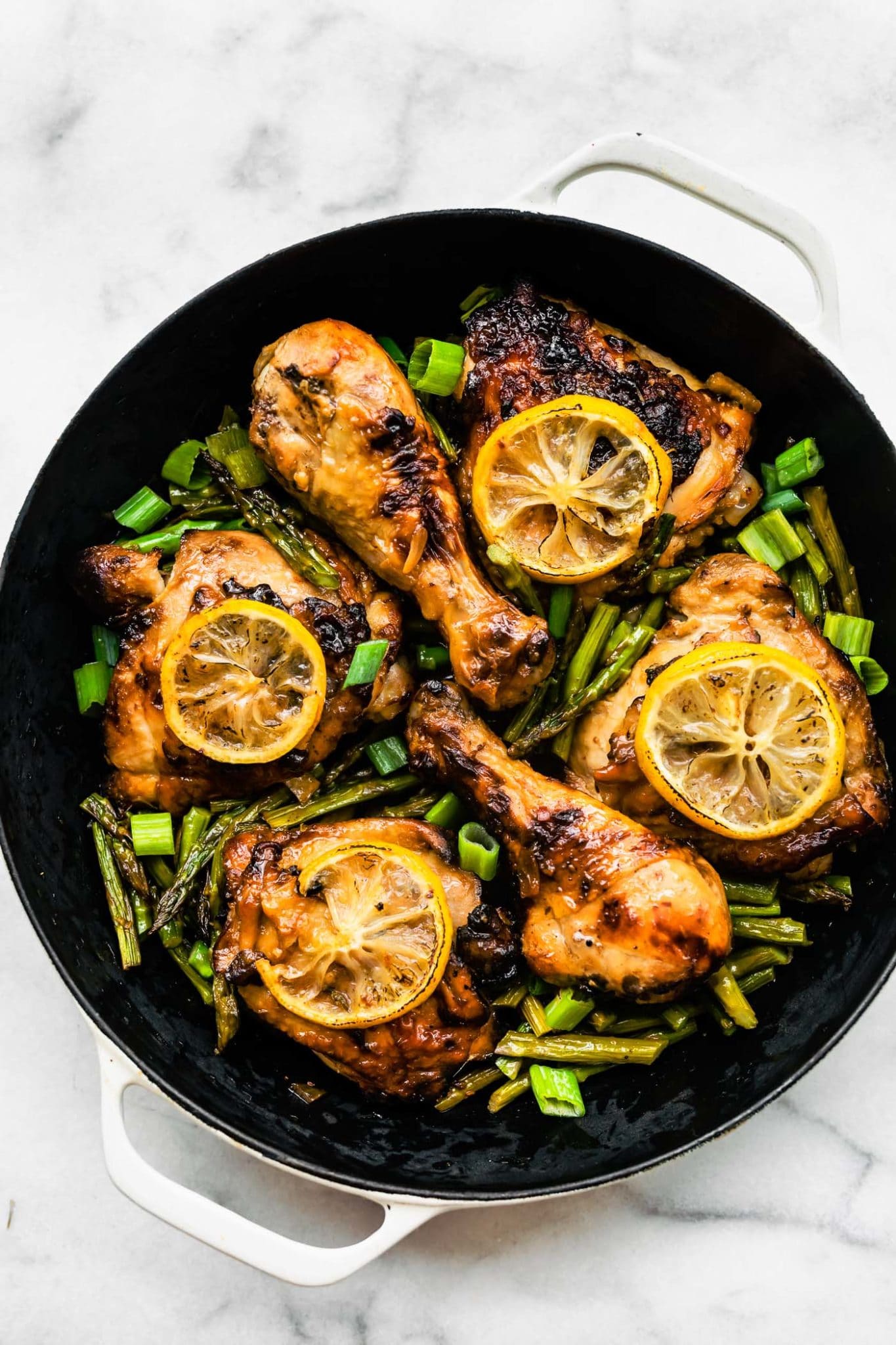 4 thighs and 2 drumsticks of honey ginger air fryer chicken in a pot on top of air fried asparagus topped with lemon slices and green onions