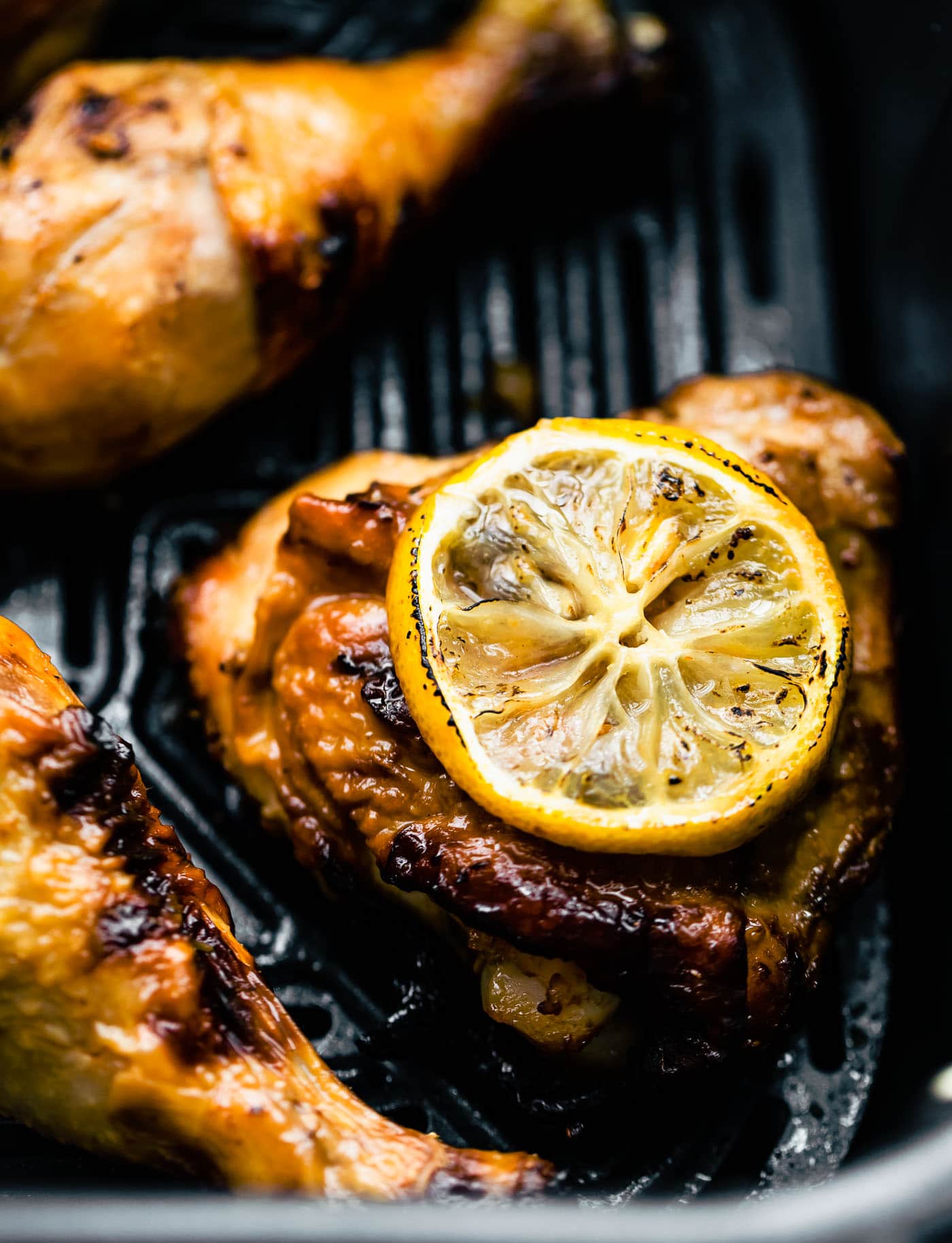 a close up image of a honey ginger air fryer chicken thigh topped with a lemon slice in the basket of an air fryer