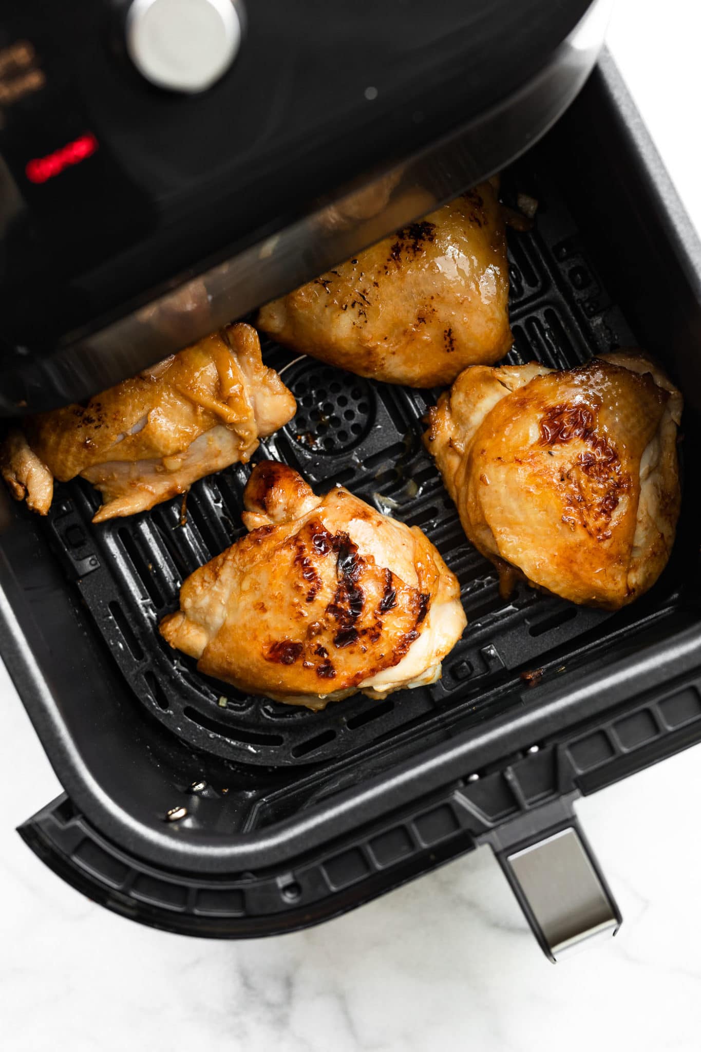 an air fryer basket halfway pulled out of an air fryer holding 4 honey ginger air fryer chicken thighs