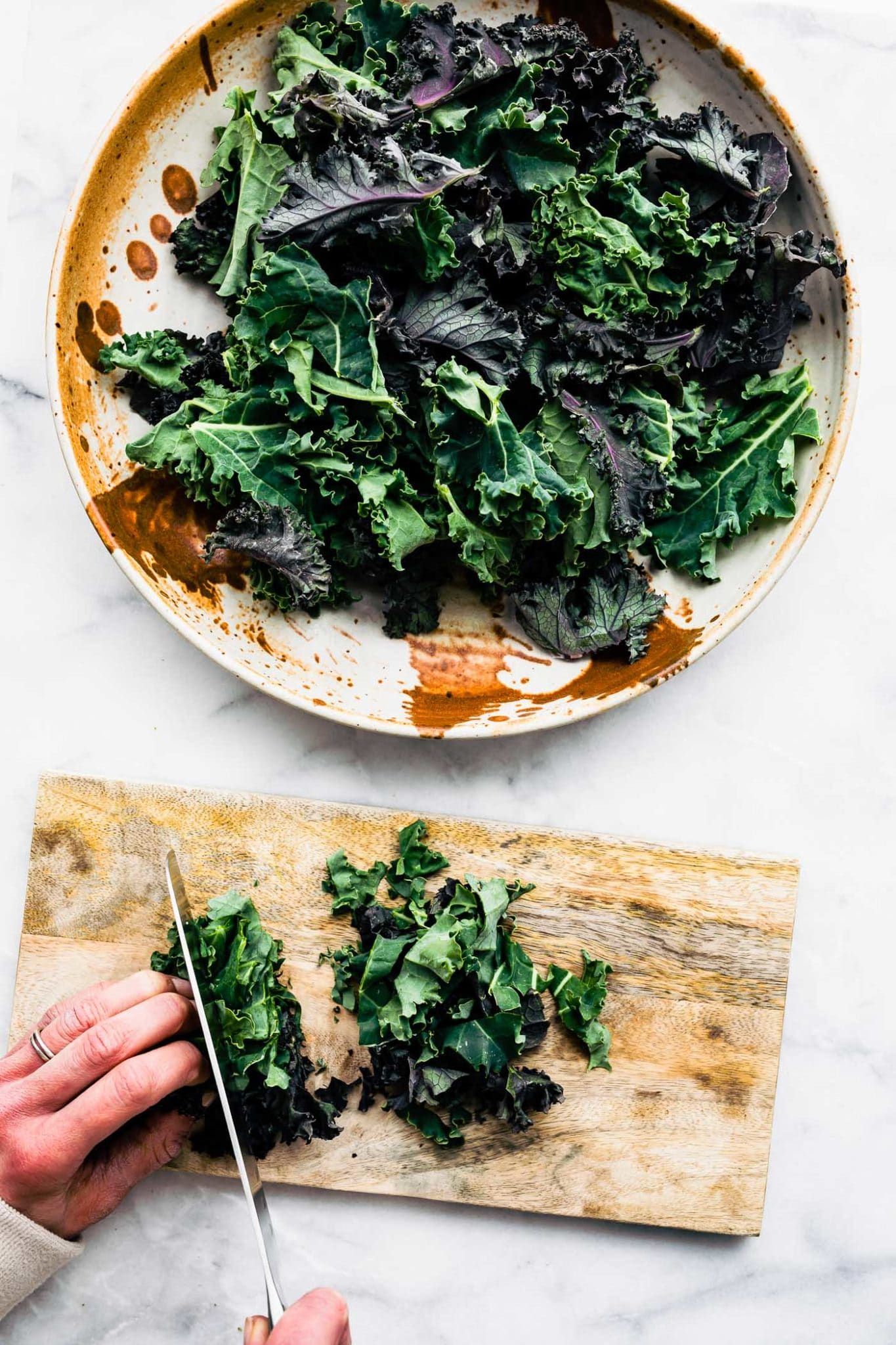 a bowl of kale leaves and a woman's hands cutting kale on a wooden cutting board