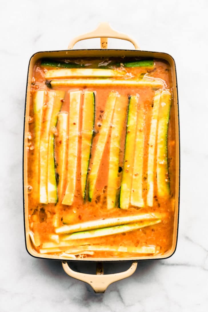 overhead image of zucchini strips covered with enchilada sauce in a casserole dish to create tex-mex egg and cauliflower casserole