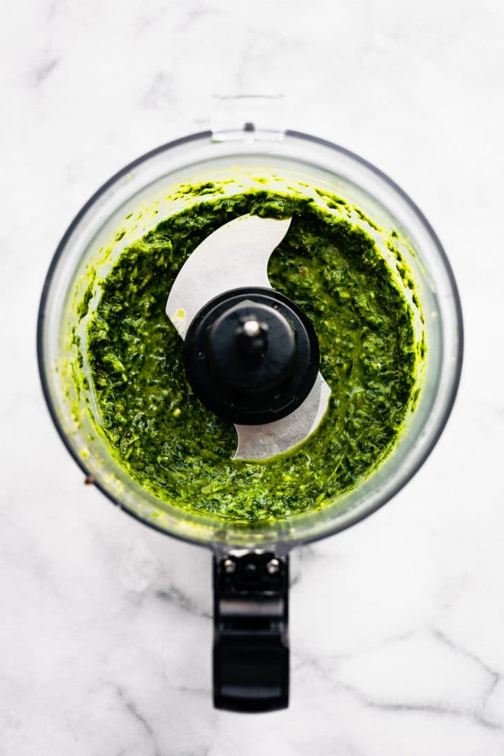 overhead image of a food processor on a white marble countertop with blended mint chimichurri sauce.