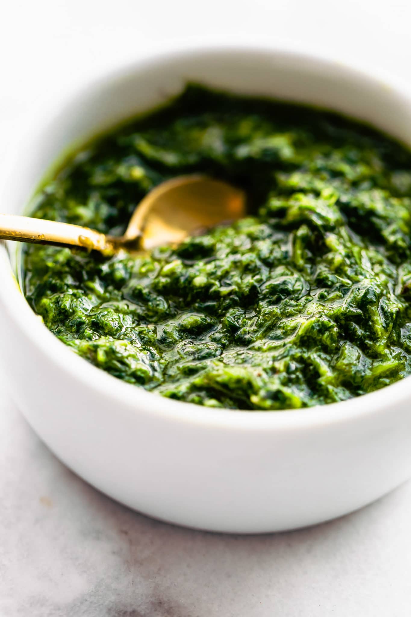 a side image of a white bowl filled with mint chimichurri sauce with a golden spoon dipped into it
