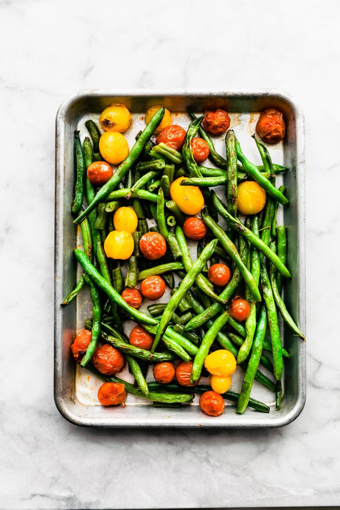 blistered cherry tomatoes and green beans in a bakin gpan