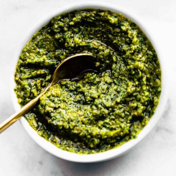 a small white bowl filled with cilantro pesto with a golden spoon dipping into the center