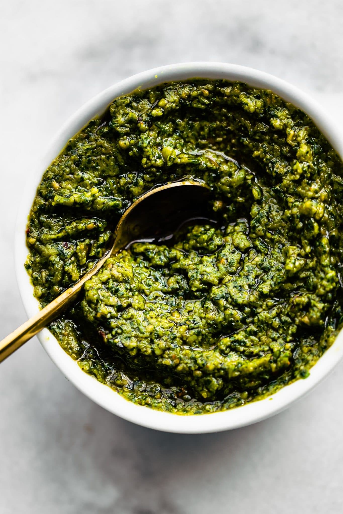 a small white bowl filled with cilantro pesto with a golden spoon dipping in the center