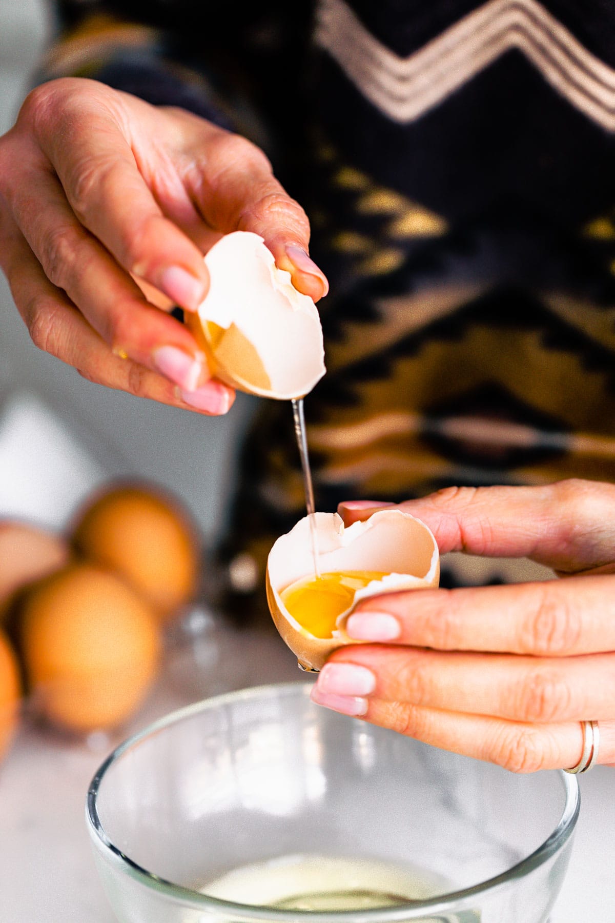 two hands holding egg a cracked egg over a glass bowl separating the yolk from the whites