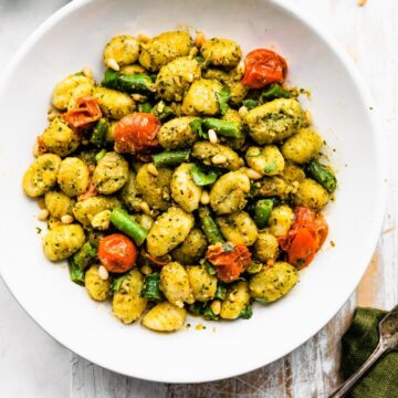 a white bowl full of gluten free gnocchi pesto pasata salad with a fork on the side