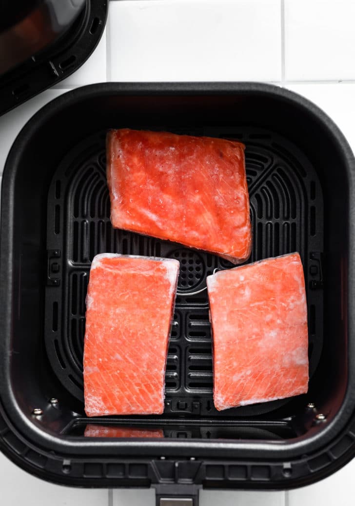 overhead photo of frozen salmon fillets in air fryer