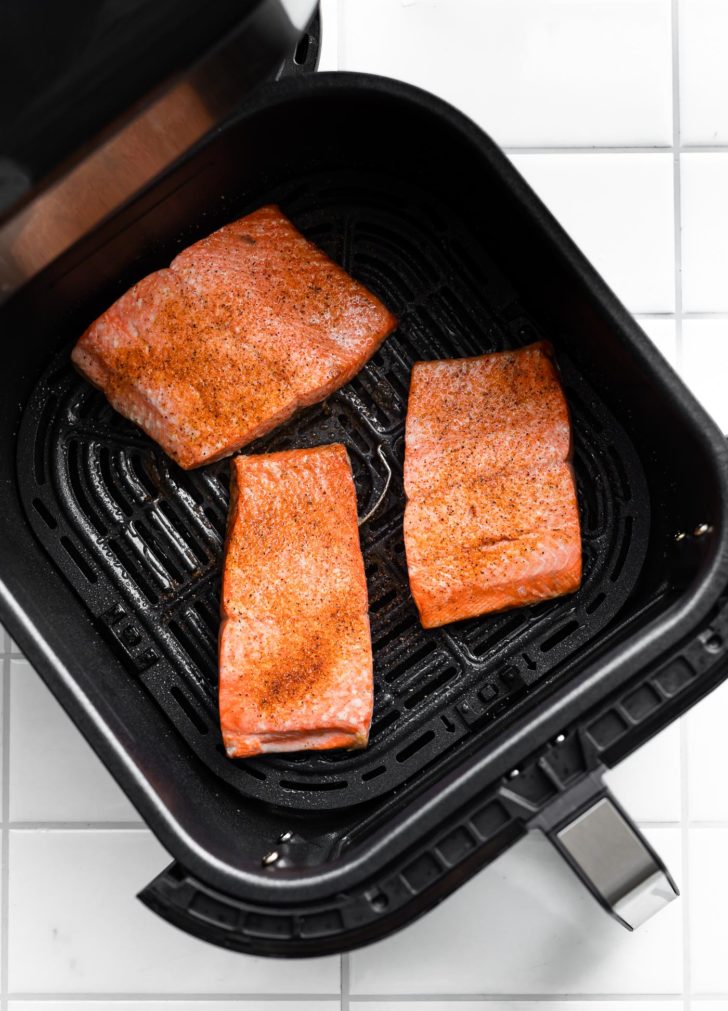 3 pieces of fresh seasoned salmon filets in the basket of an air fryer ready to be cooked