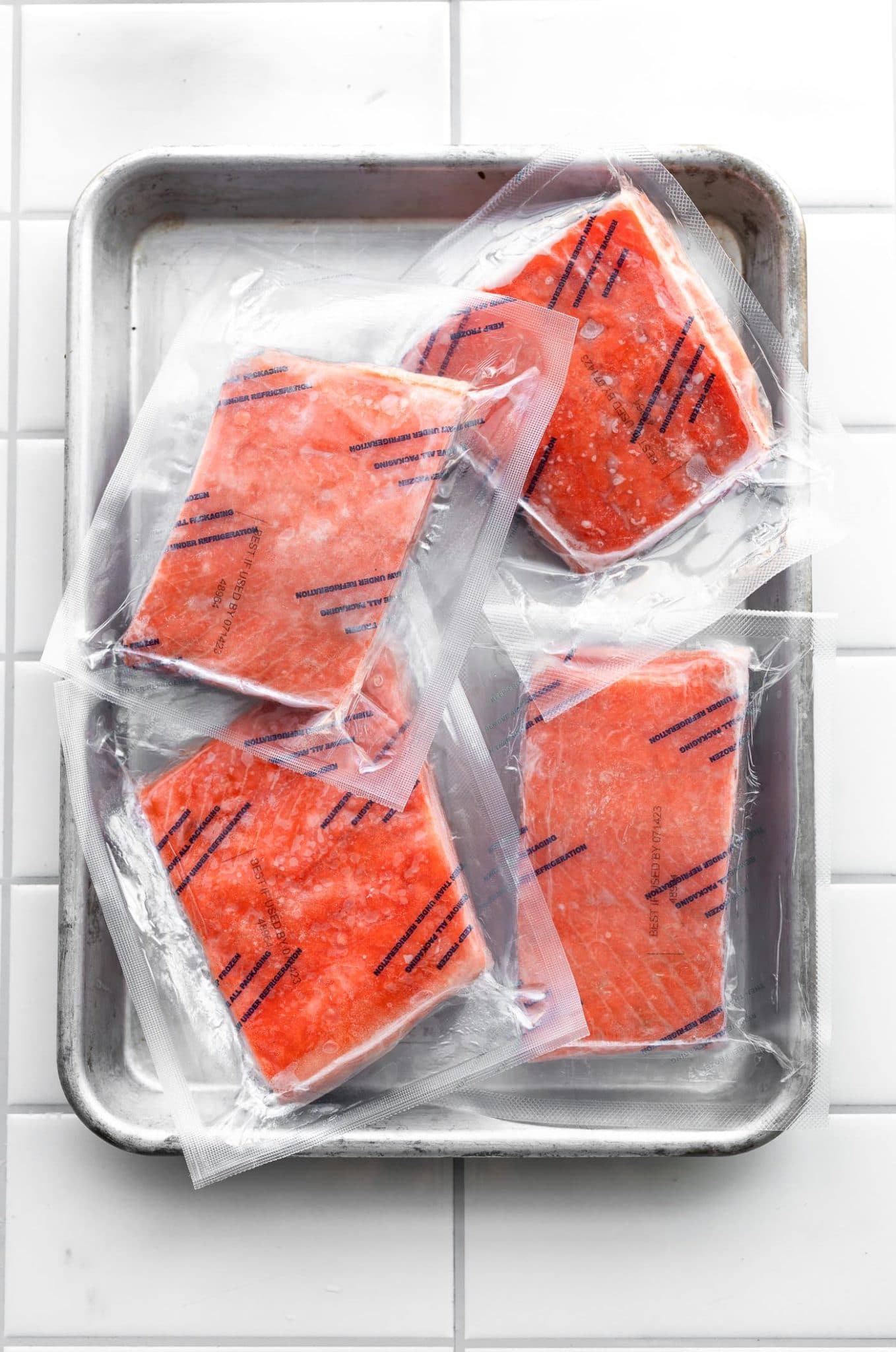 4 pieces of frozen salmon in individual sealed plastic bags sitting in a baking dish