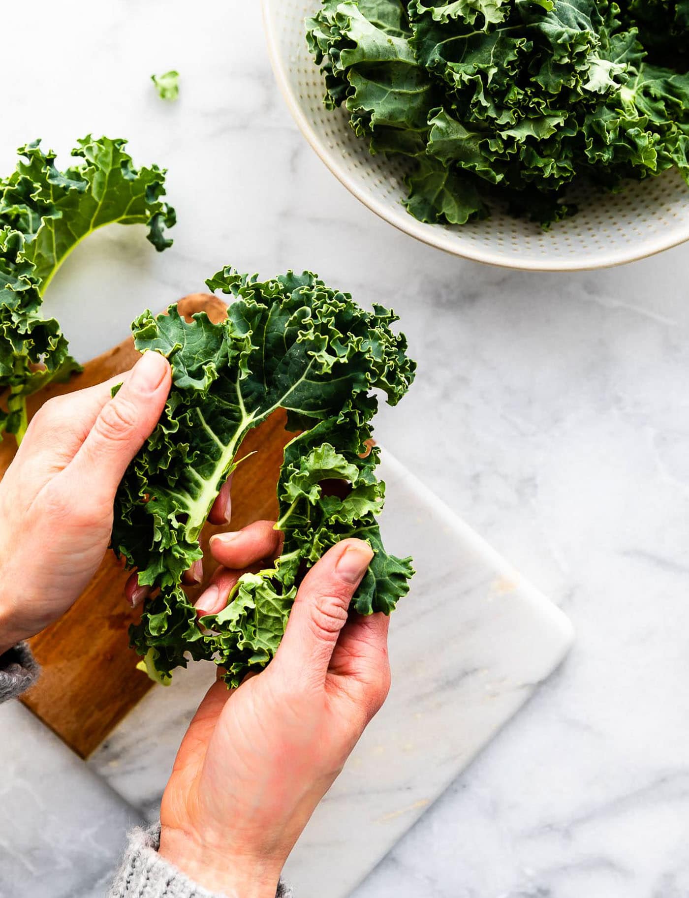 a woman's hands pulling kale leaves off a rib of kale