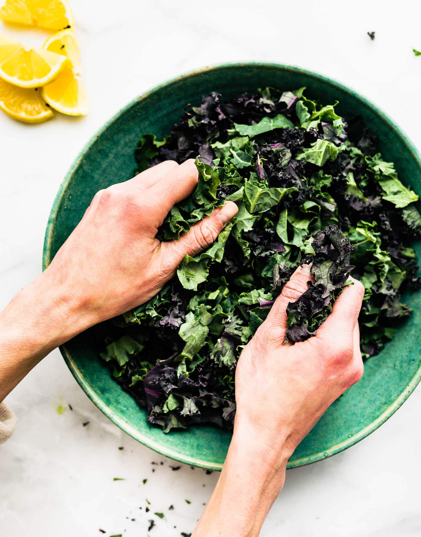 a woman's hands massaging kale in a blue bowl with lemon wedges off to the side