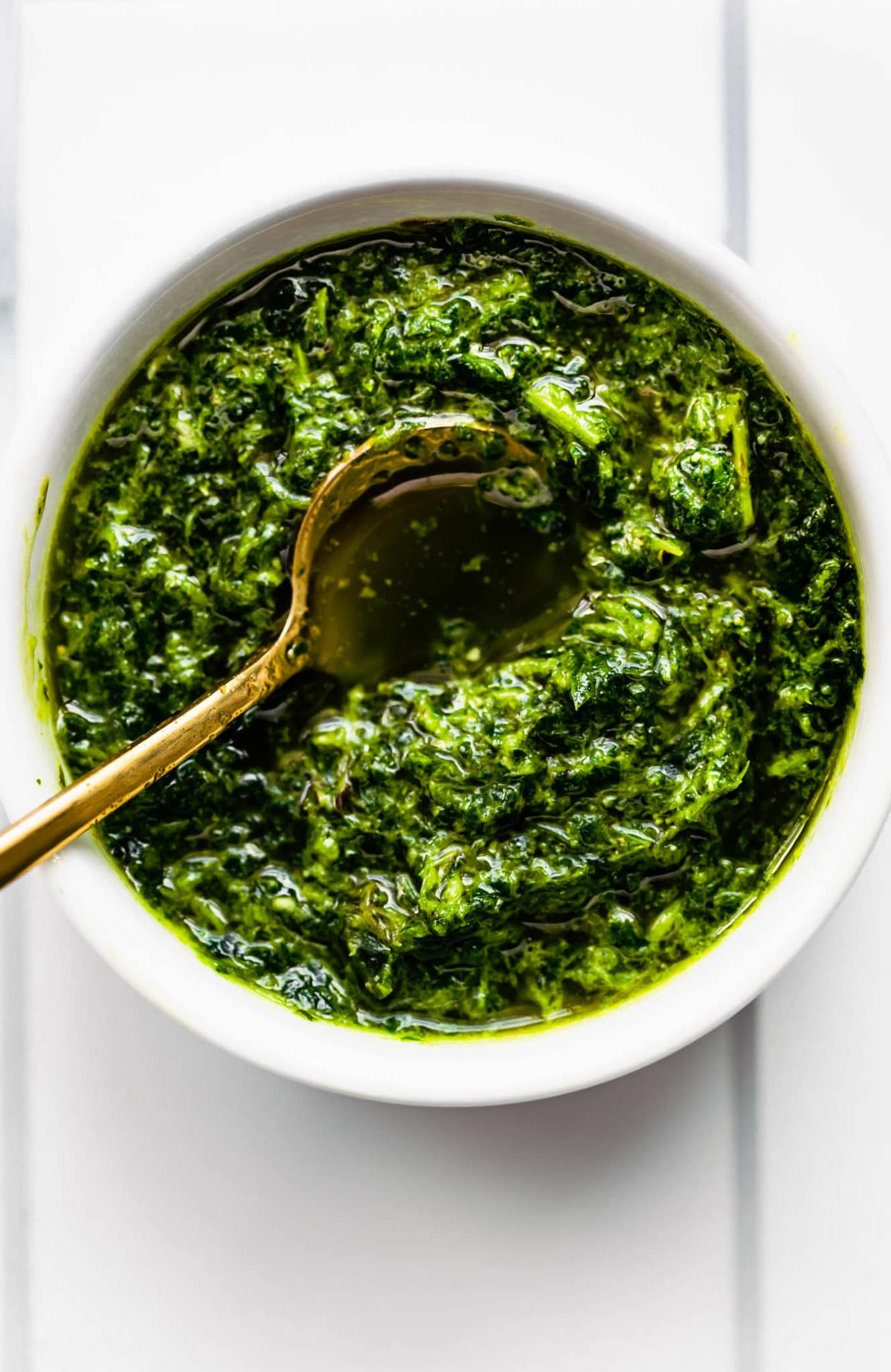 a white bowl filled with mint chimichurri sauce with a golden spoon dipped in the center