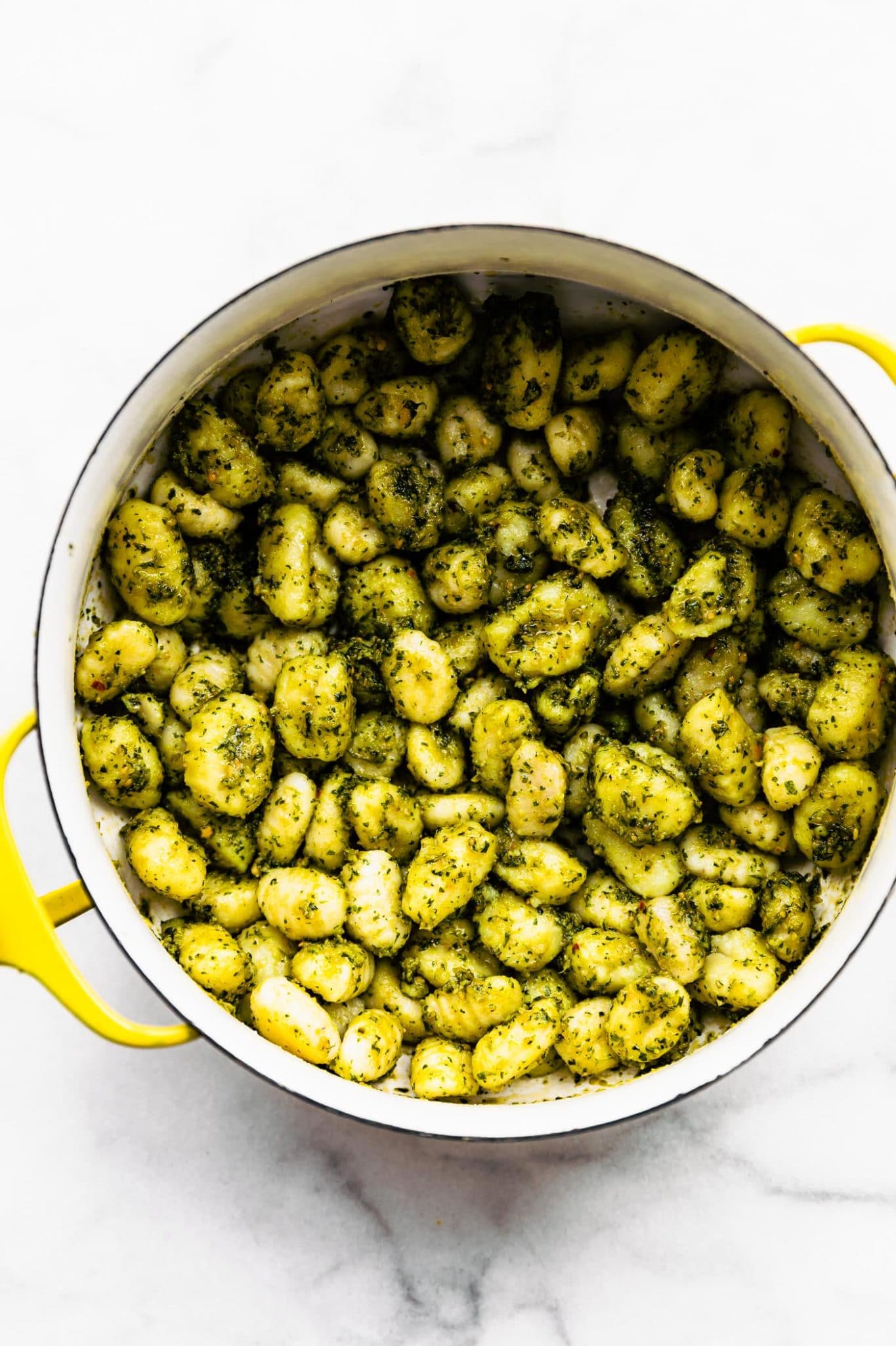 overhead image of gluten free gnocchi coated with pesto sauce in a yellow pot