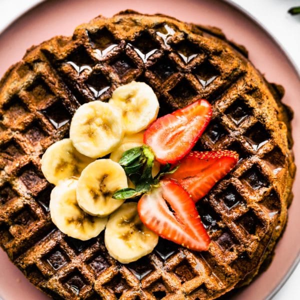 overhead shot of waffles on pink plate with banana and strawberry on top