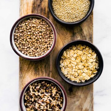 four bowls of gluten free grains on a wooden plank containing buckwheat, millet, gluten free oats, and quinoa
