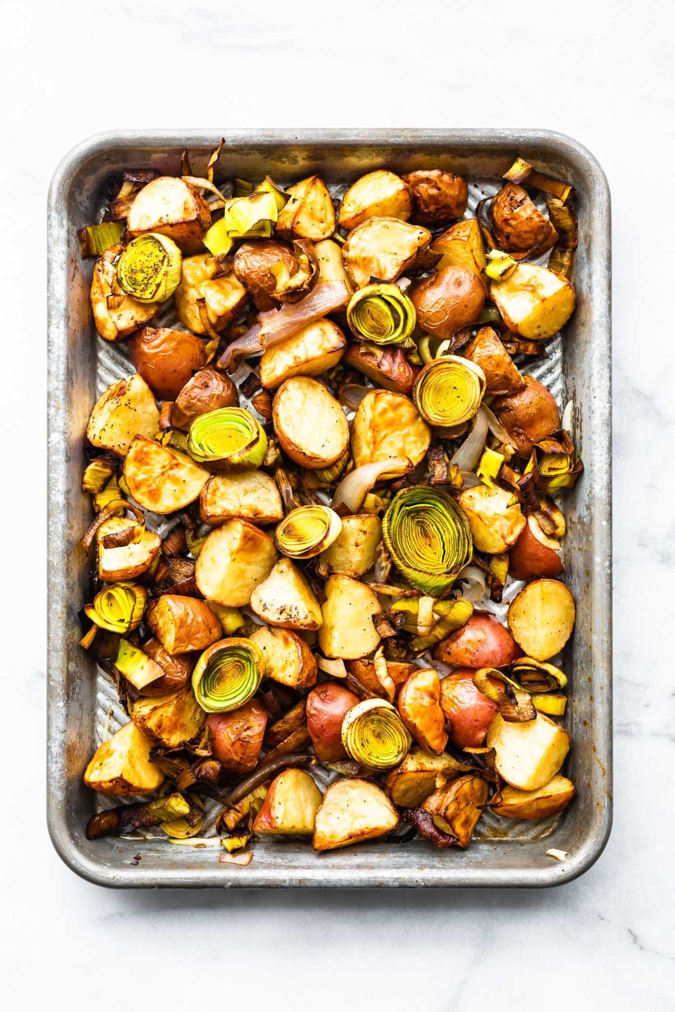 an overhead image of a sheet pan full of roasted leeks and potatoes with onions