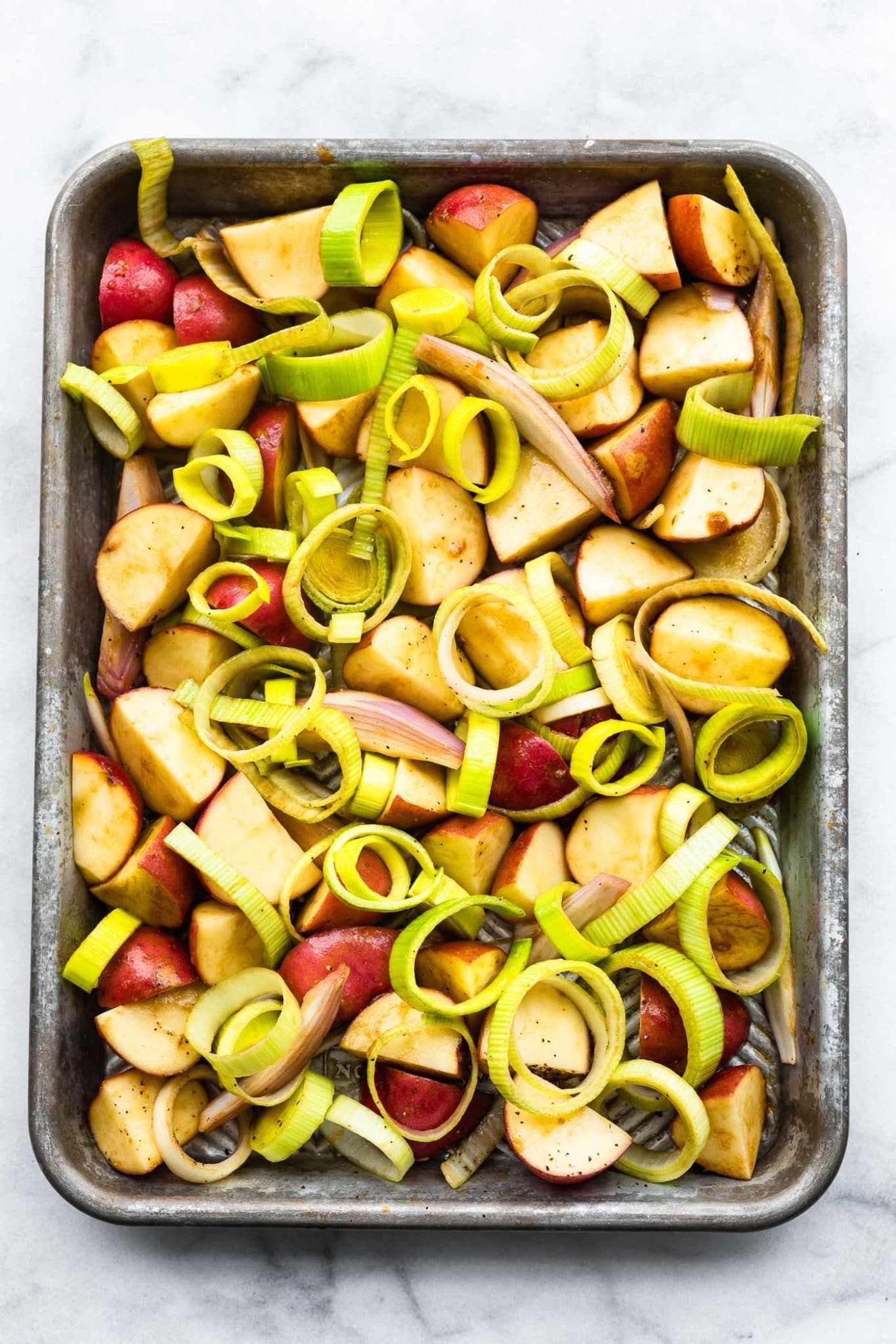 a sheet pan full of raw red onions, red potatoes, and leeks sliced into rings