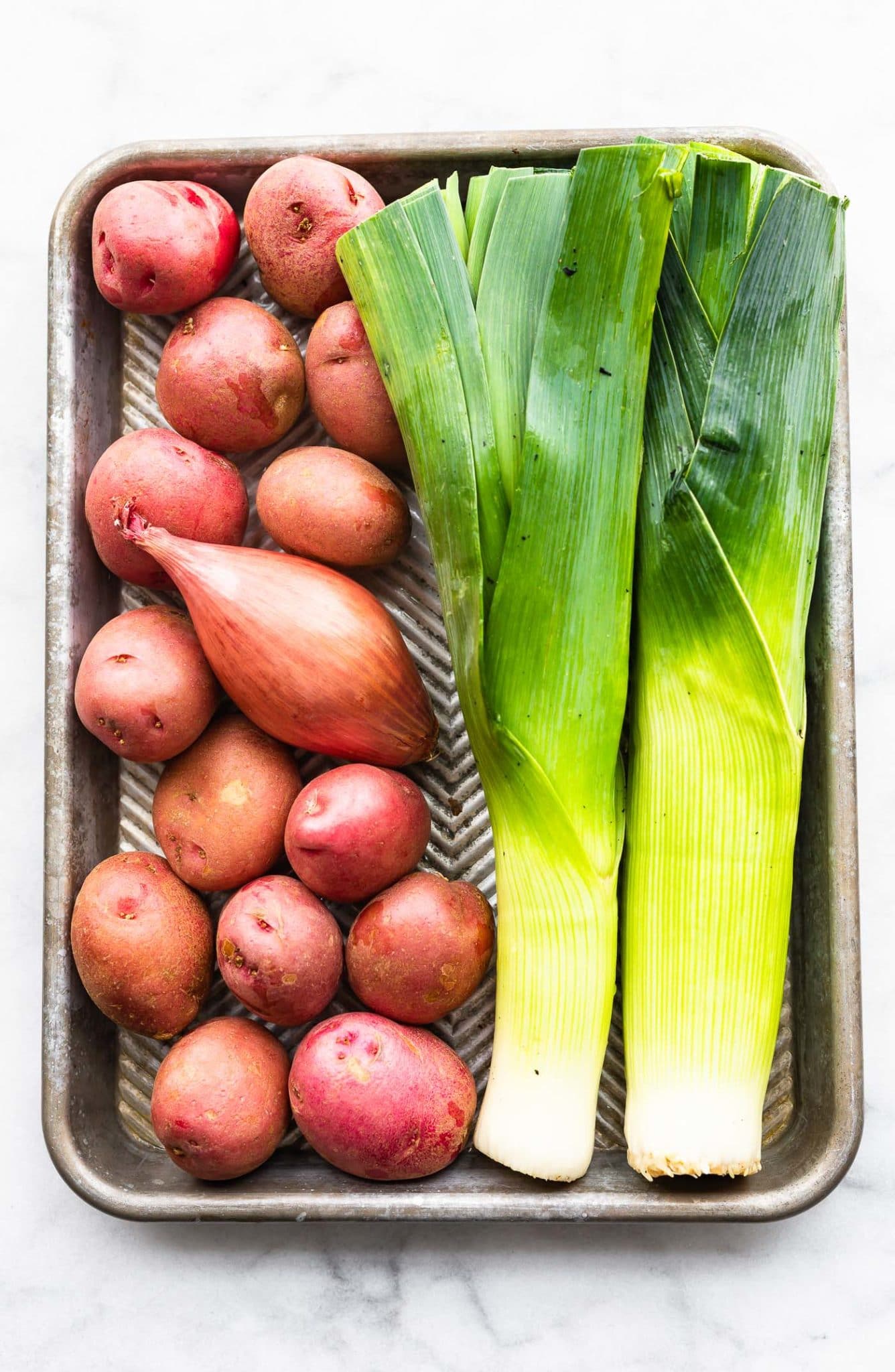 a sheet pan holding raw whole red onions, a full shallot, and two leeks