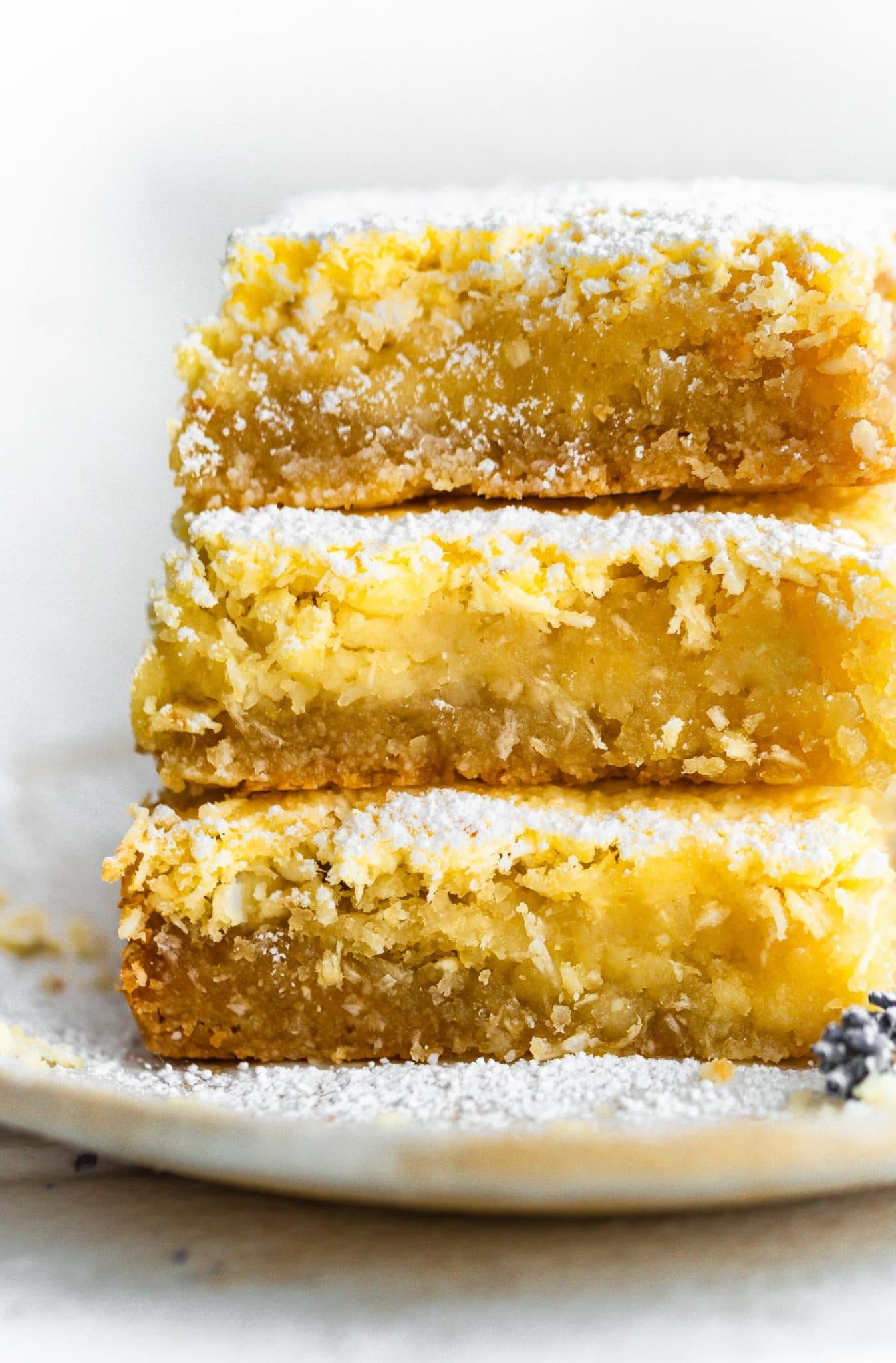 three gluten free lemon bars with coconut stacked on top of each other on a plate