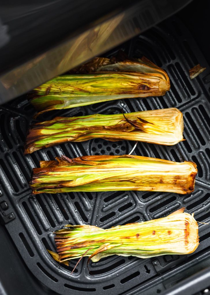 four leeks in an air fryer basket with charred marks from being roasted