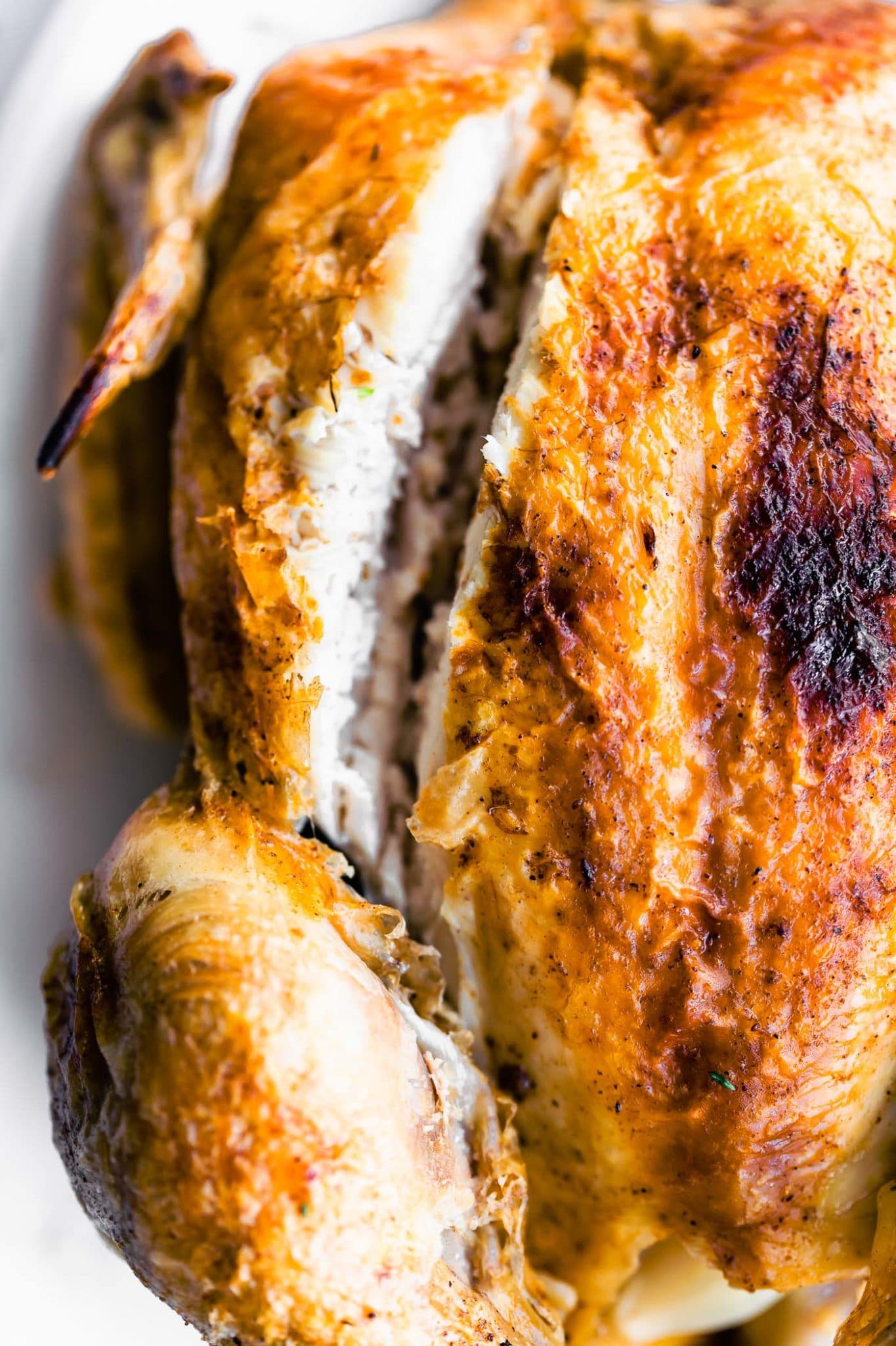close up image of a whole chicken with extra crispy skin with a slice on the side 