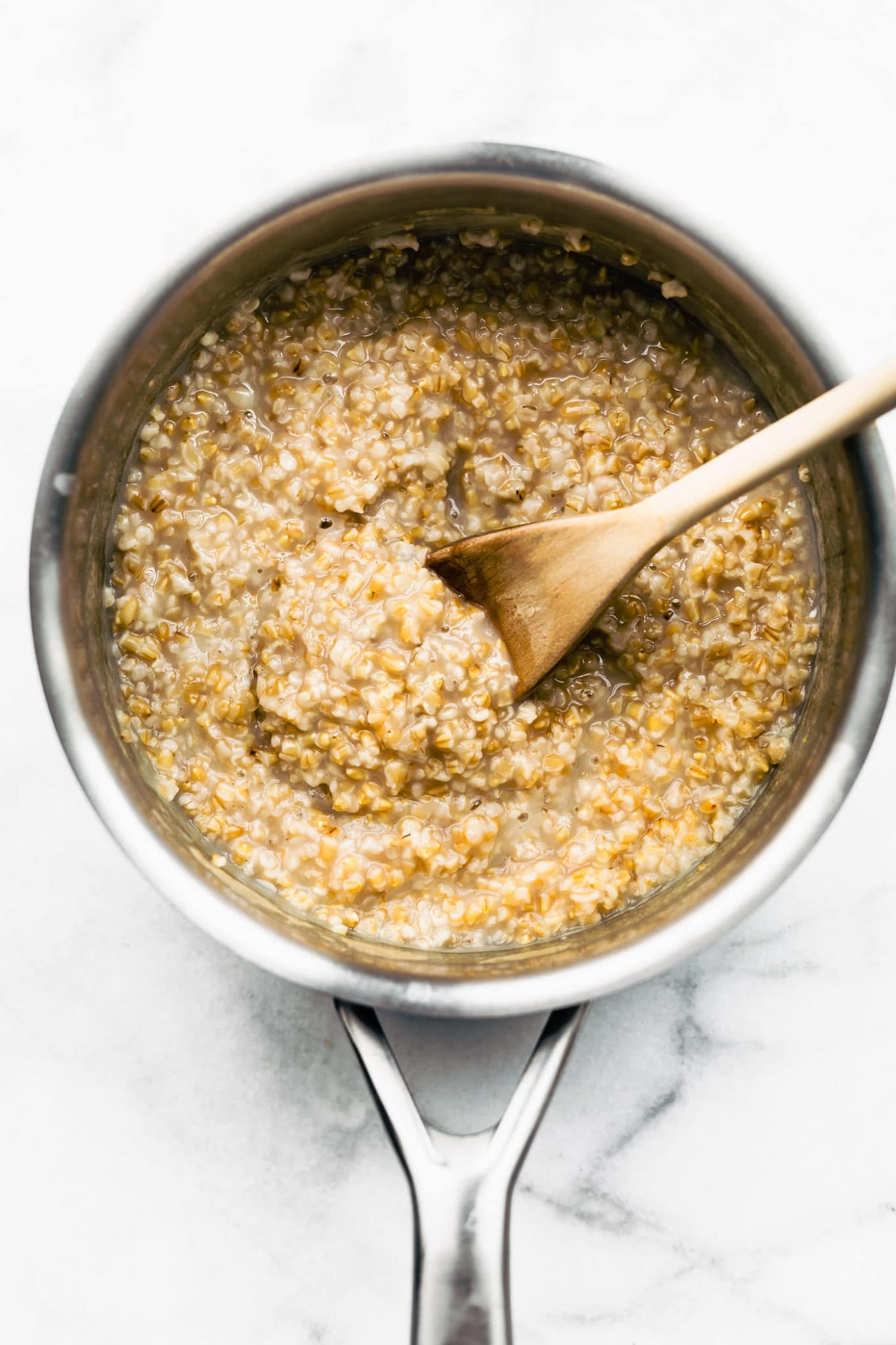overhead image of cooked oats in a sauce pan being stirred with a wooden spoon