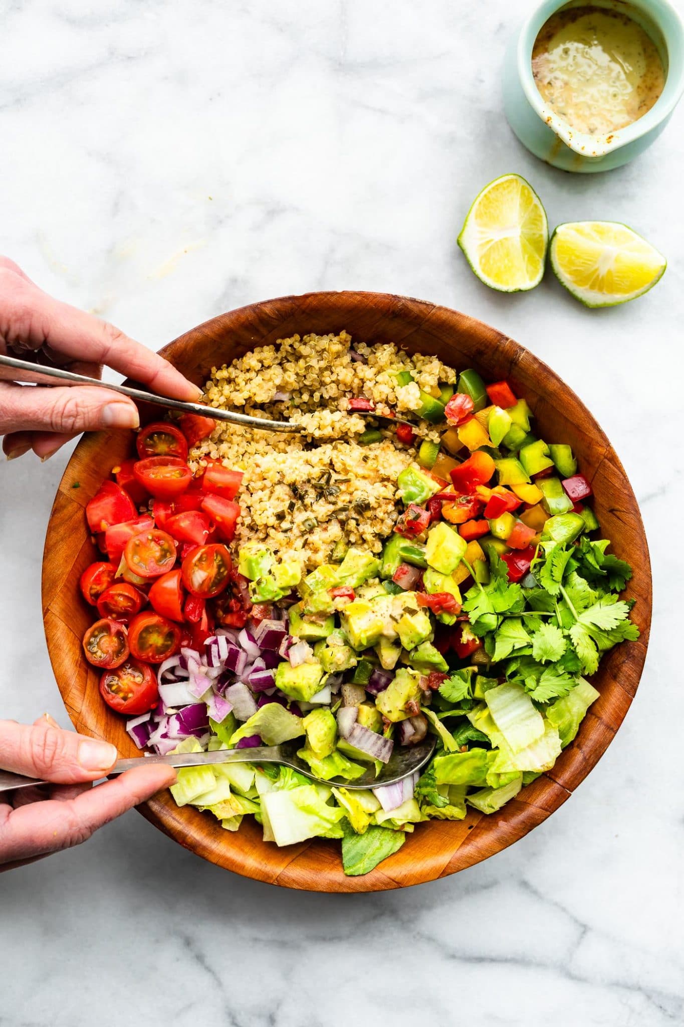 Two hands holding serving spoons tossing together Fiesta Quinoa Salad
