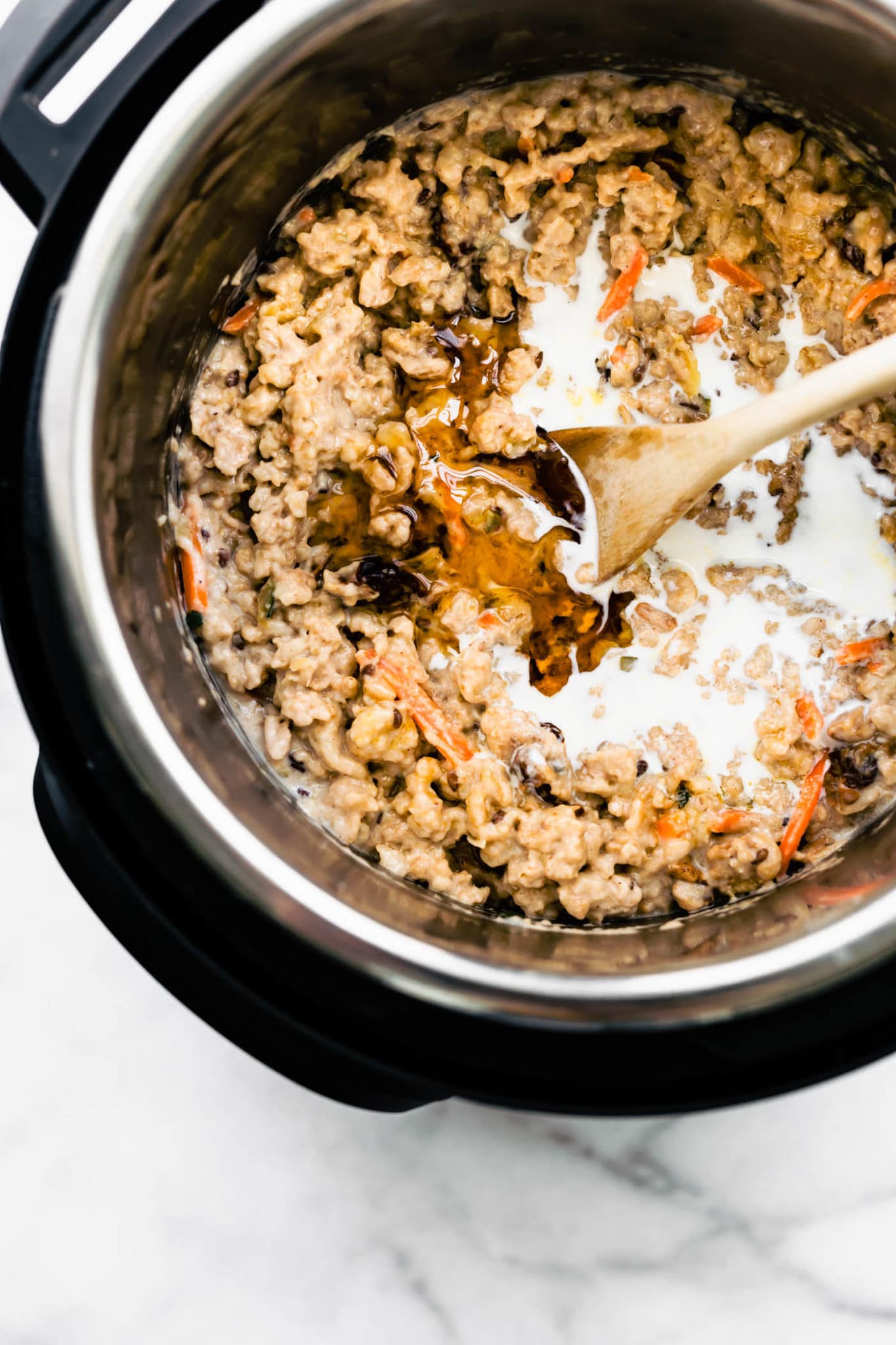 overhead image of superfood instant pot oatmeal in an instant pot with carrots, nuts, honey, and milk being stirred with a wooden spoon