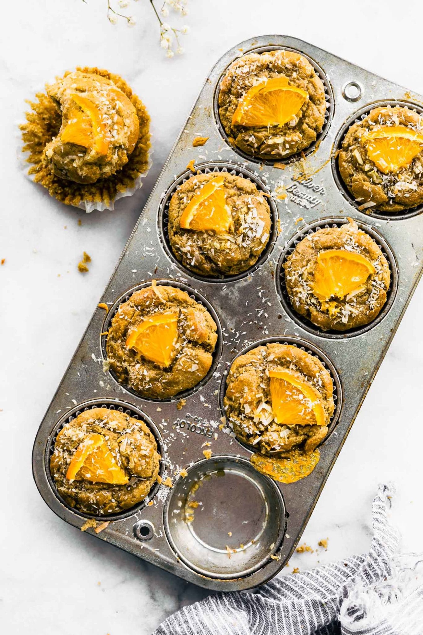 orange oat coconut muffins in muffin tin with one muffin bitten into